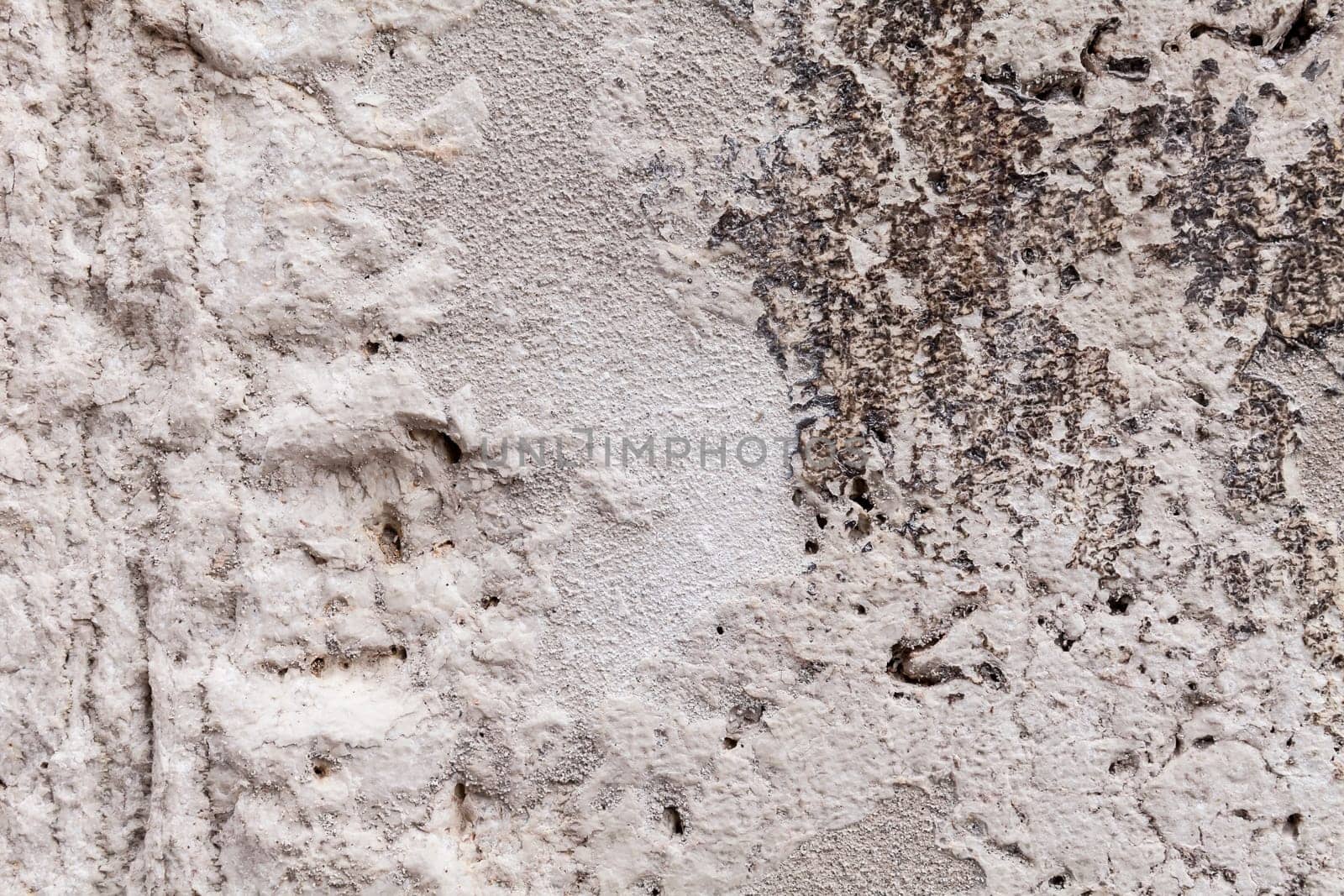Rough texture of an ancient block of stone part of an external wall. Cavernous rock structure with brittle surface. Pale gray and beige colors with dark streaks. Close up shot outdoors on a tripod.