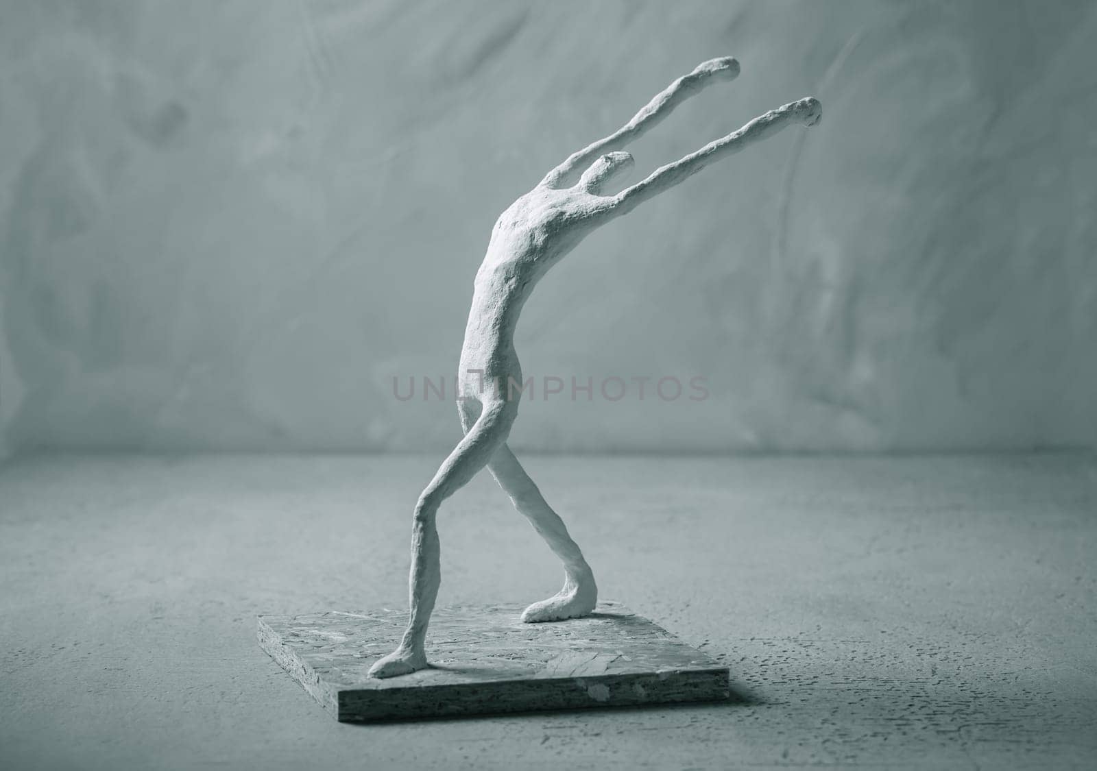 Plaster sculpture of sportsman in winner pose on concrete background in grey tones.