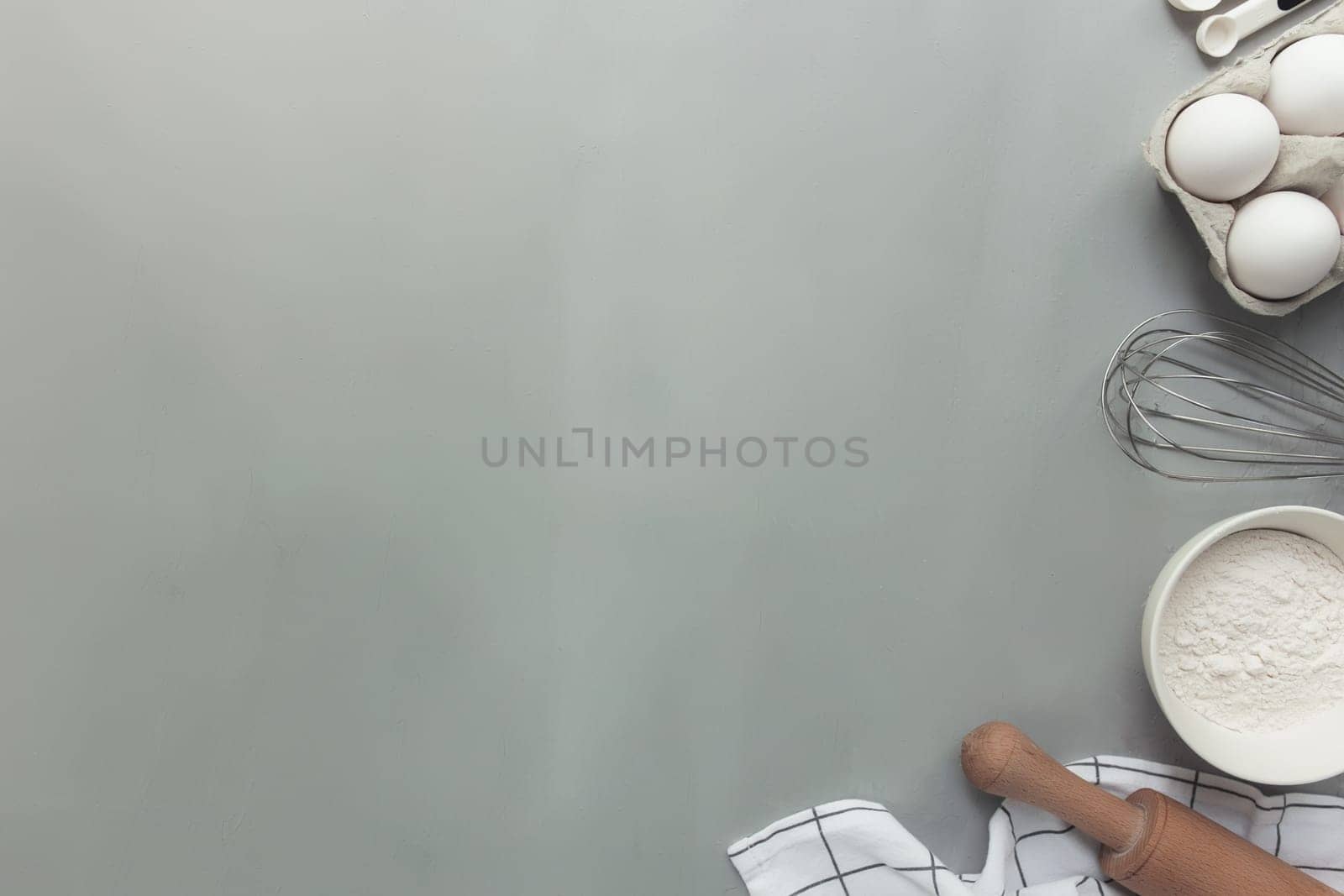 Baking ingredients, kitchen utensils, cooking concept on grey background flat lay, copy space. Prepare dough, egg, bowl flour, rolling pin, whisk, kitchen towel, salt, soda. Kitchen as a hobby