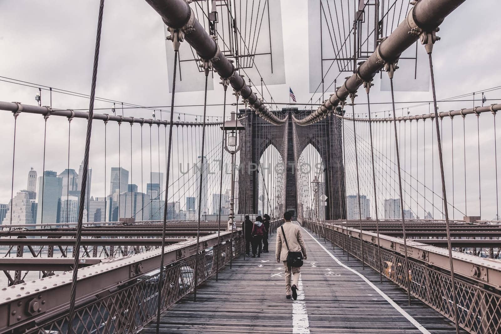 Man walking on pedestrian path across Brooklyn bridge. New York City Manhattan downtown with skyscrapers over East River panorama as seen from Brooklyn bridge.
