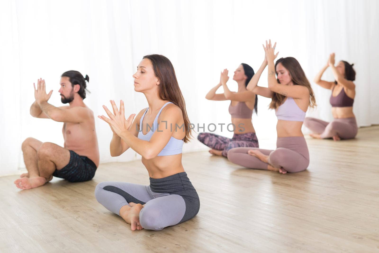 Group of young authentic sporty attractive people in yoga studio, practicing yoga lesson with instructor. Healthy active lifestyle, working out in gym.