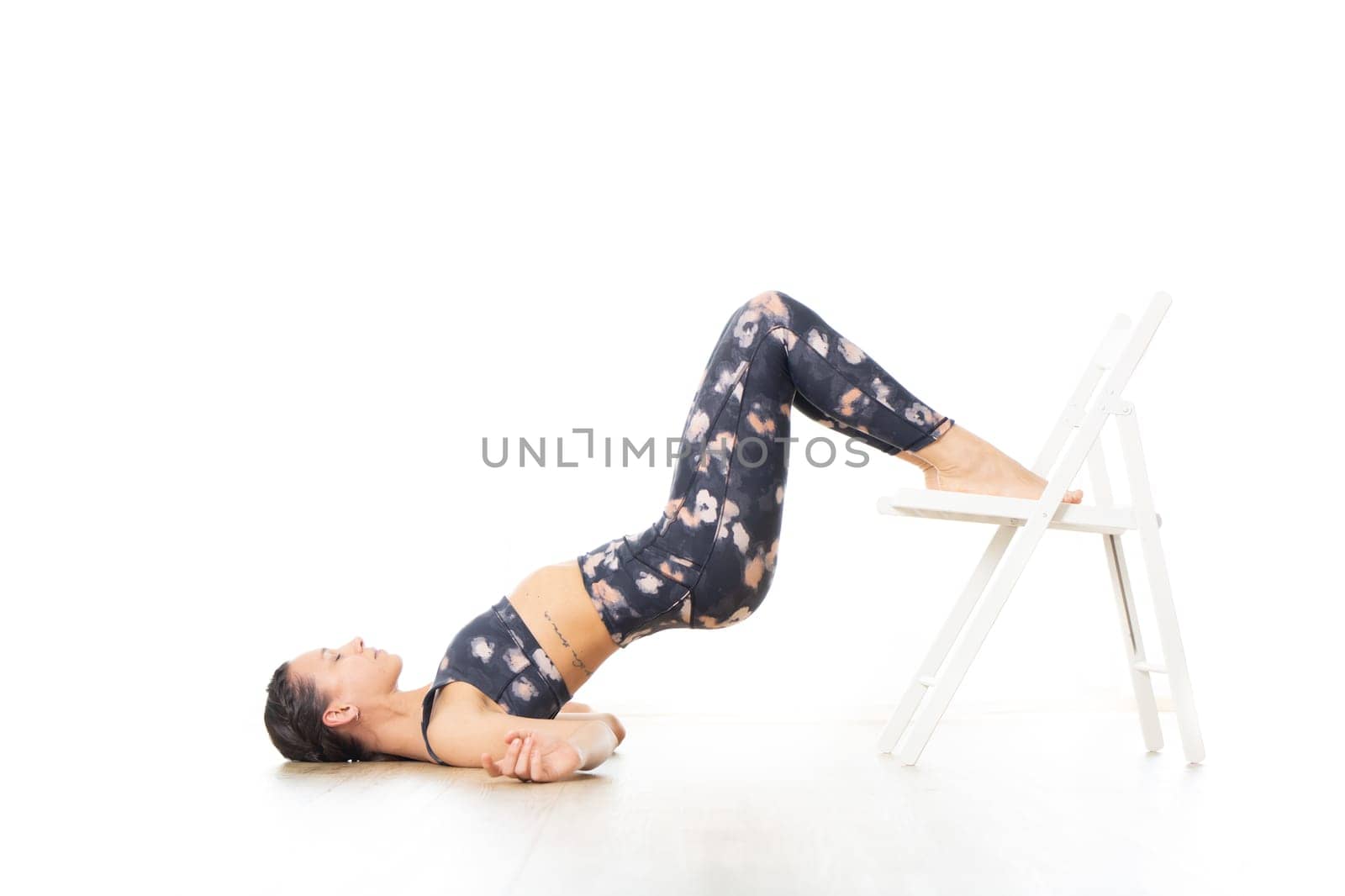 Young sporty attractive woman in bright white yoga studio, stretching and relaxing during restorative yoga using white chair as a gadget. Healthy active lifestyle.