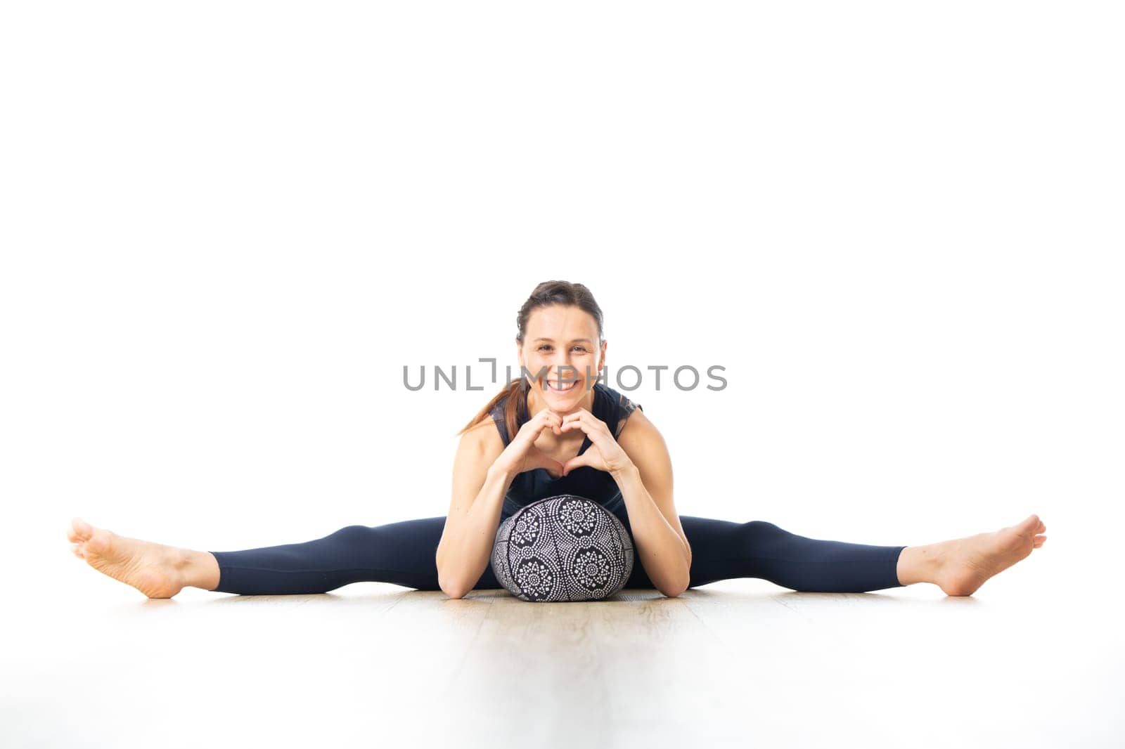 Restorative yoga with a bolster. Young sporty female yoga instructor in bright white yoga studio, lying on bolster cushion, stretching, smilling, showing love and passion for restorative yoga.