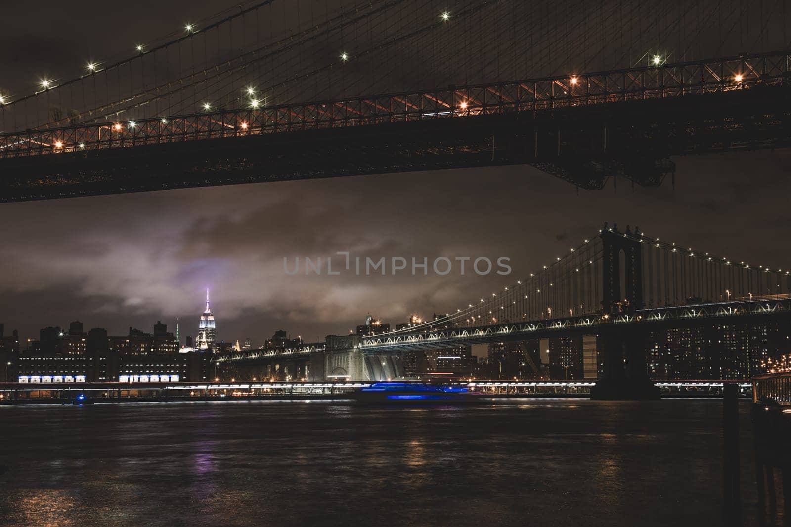 Manhattan bridge and New York City downtown skyline at dusk with skyscrapers illuminated over East River panorama. Copy space.