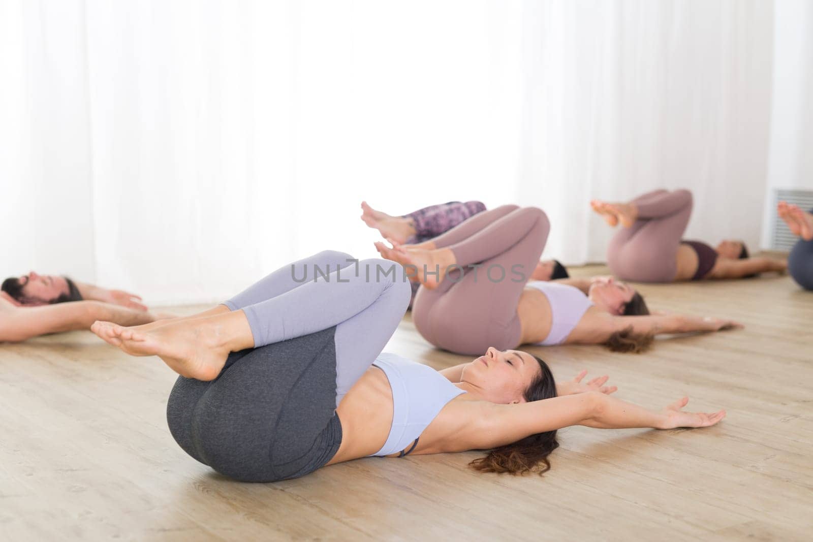 Group of young authentic sporty attractive people in yoga studio, practicing yoga lesson with instructor. Healthy active lifestyle, working out in gym.