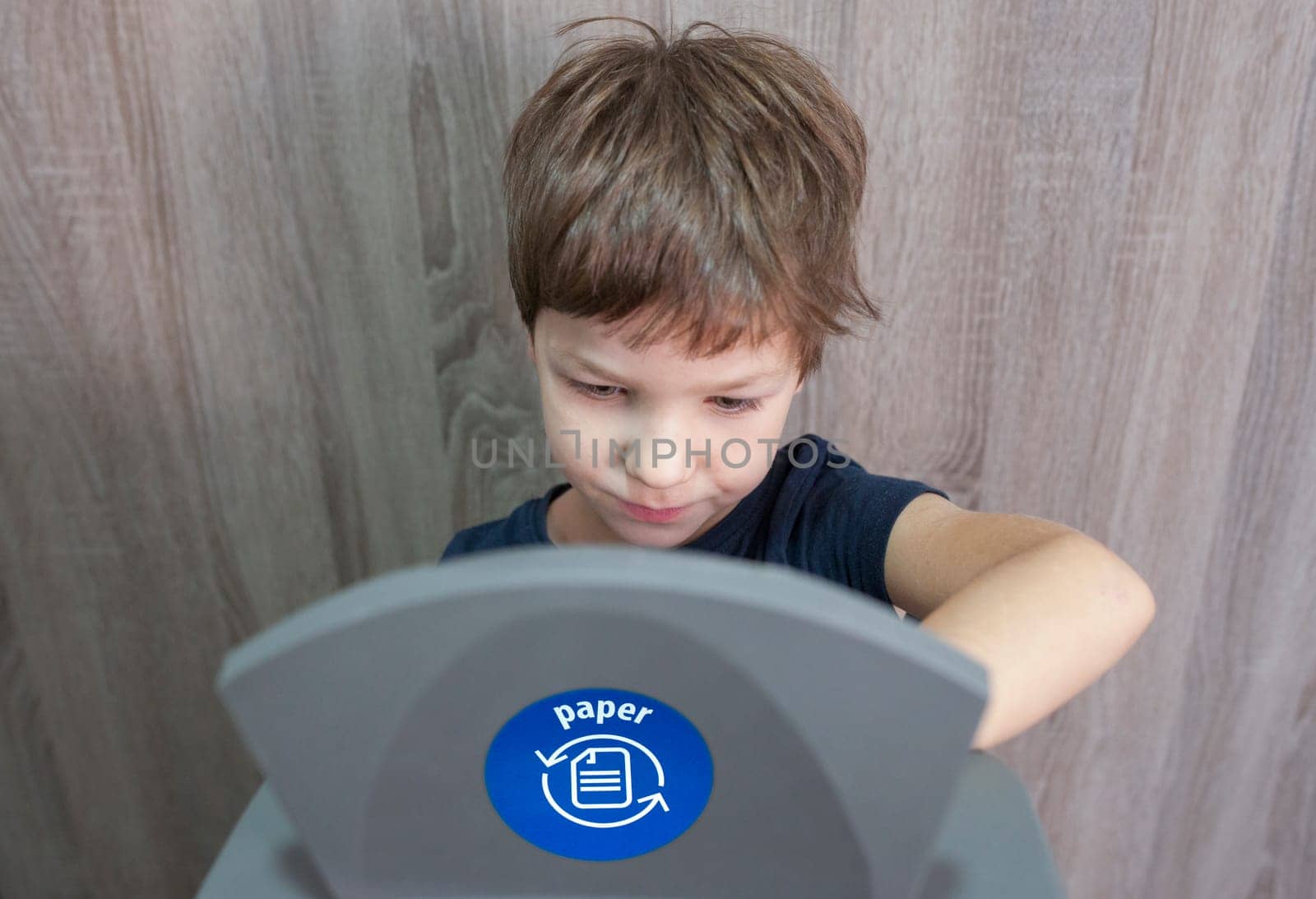Child boy throwing paper to waste bin for paper at home. Education about waste segregation concept