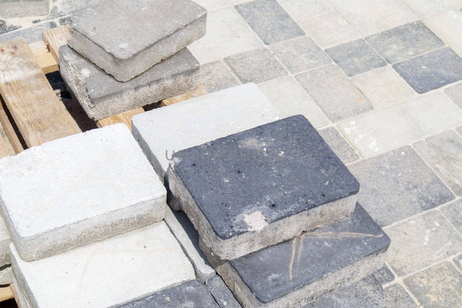 Concrete or paved gray paving slabs or floor or walkway stones stacked on a pallet. Concrete paving slabs in the backyard or road paving. Garden brick path in the courtyard on a sandy foundation