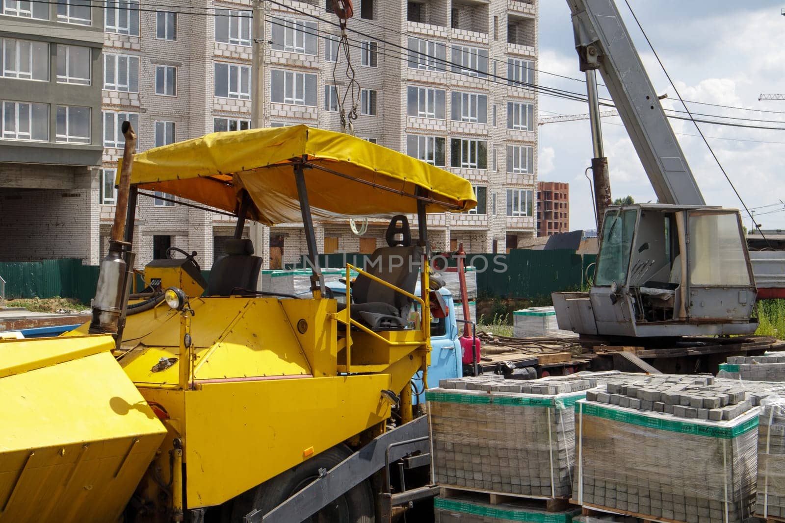 An asphalt paver is parked at a construction site. Road construction machinery stands by the road in a warehouse. Construction of heavy roads and repair of city streets