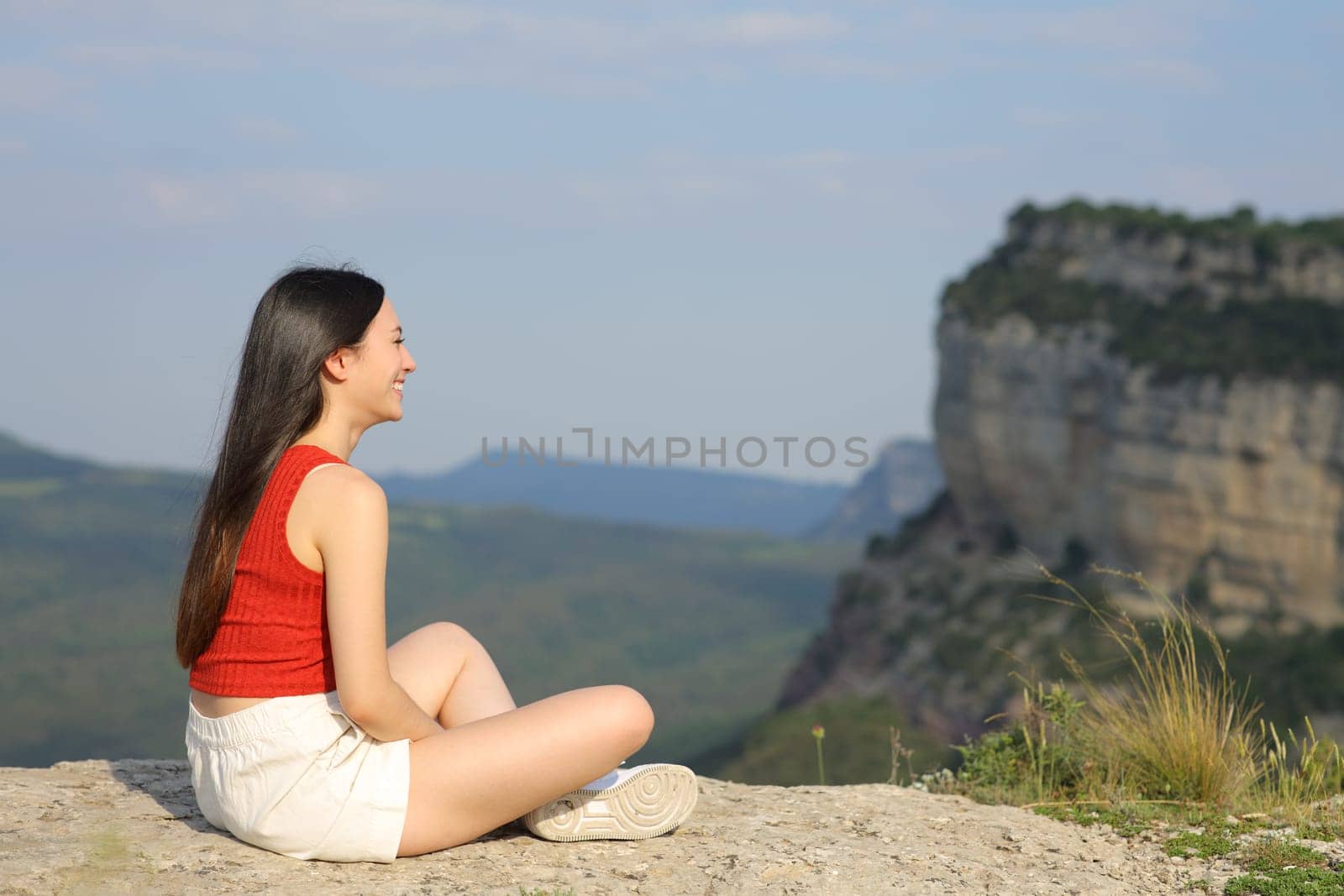 Full body portrait of an asian woman contemplating views sitting in a mountain cliff