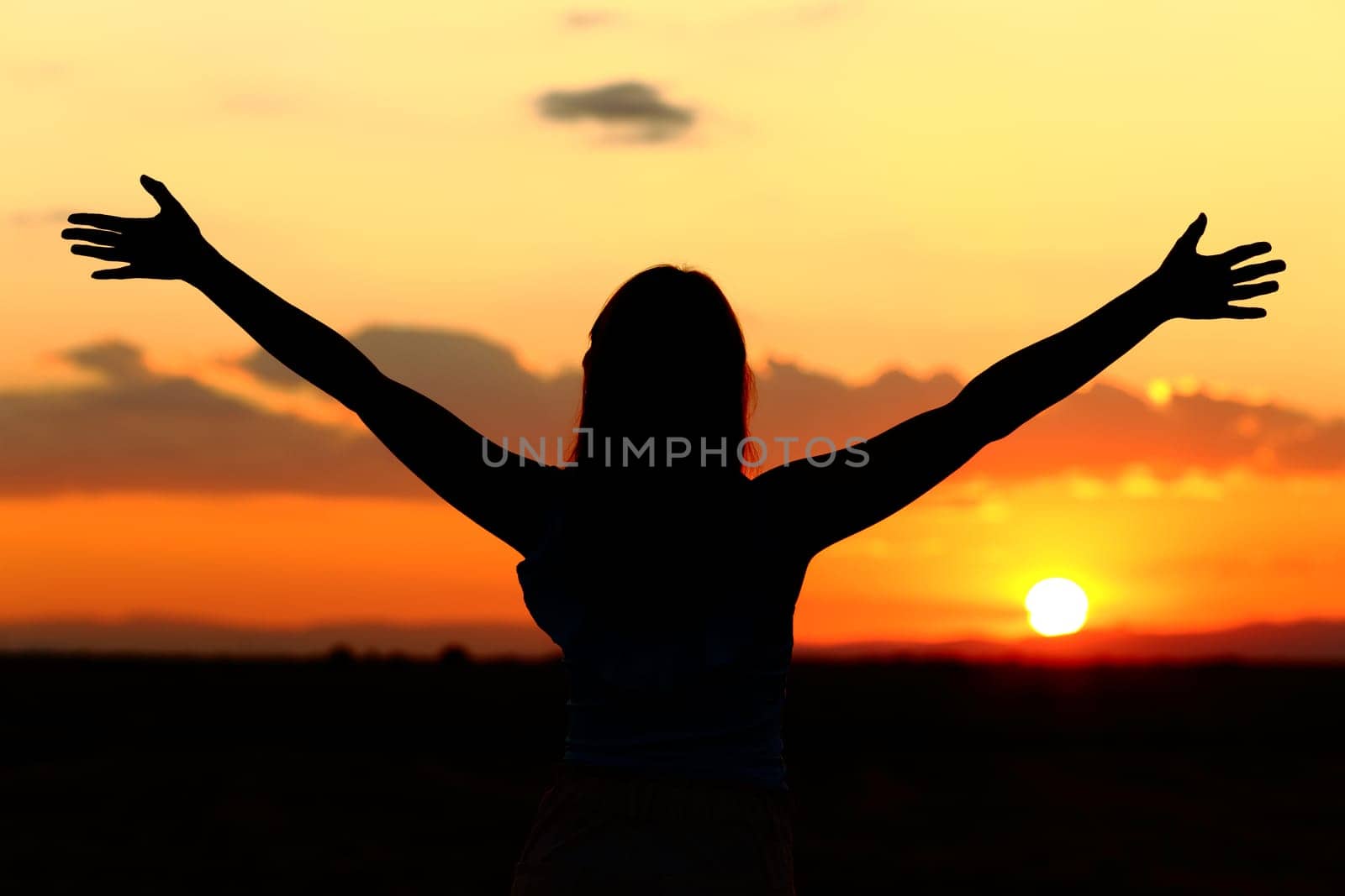 Woman silhouette celebrating stretching arms at sunset
