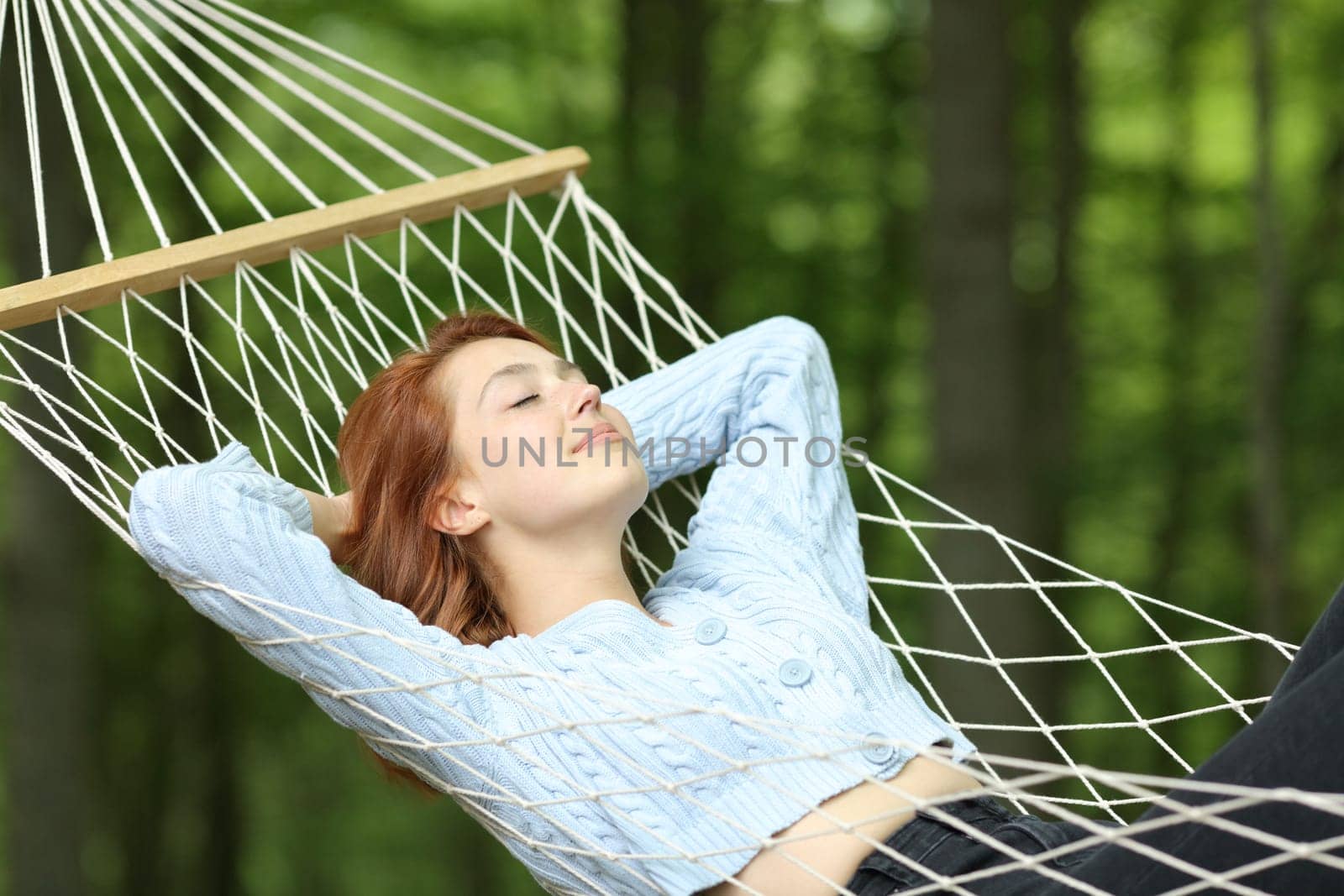 Woman relaxing lying on rope hammock in a forest on summer vacation