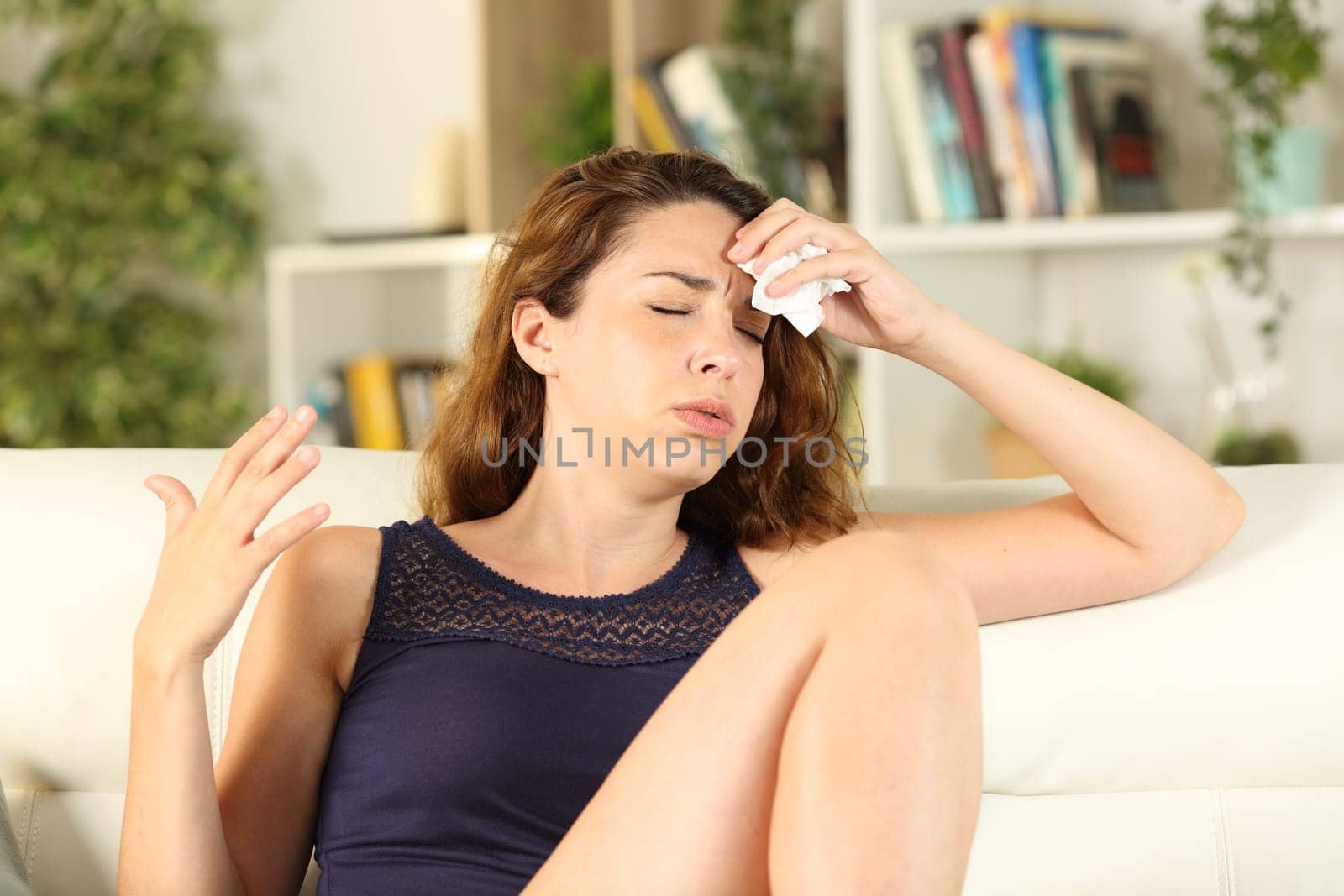 Woman complaining suffering heat stroke drying sweat sitting on a sofa in the living room at home