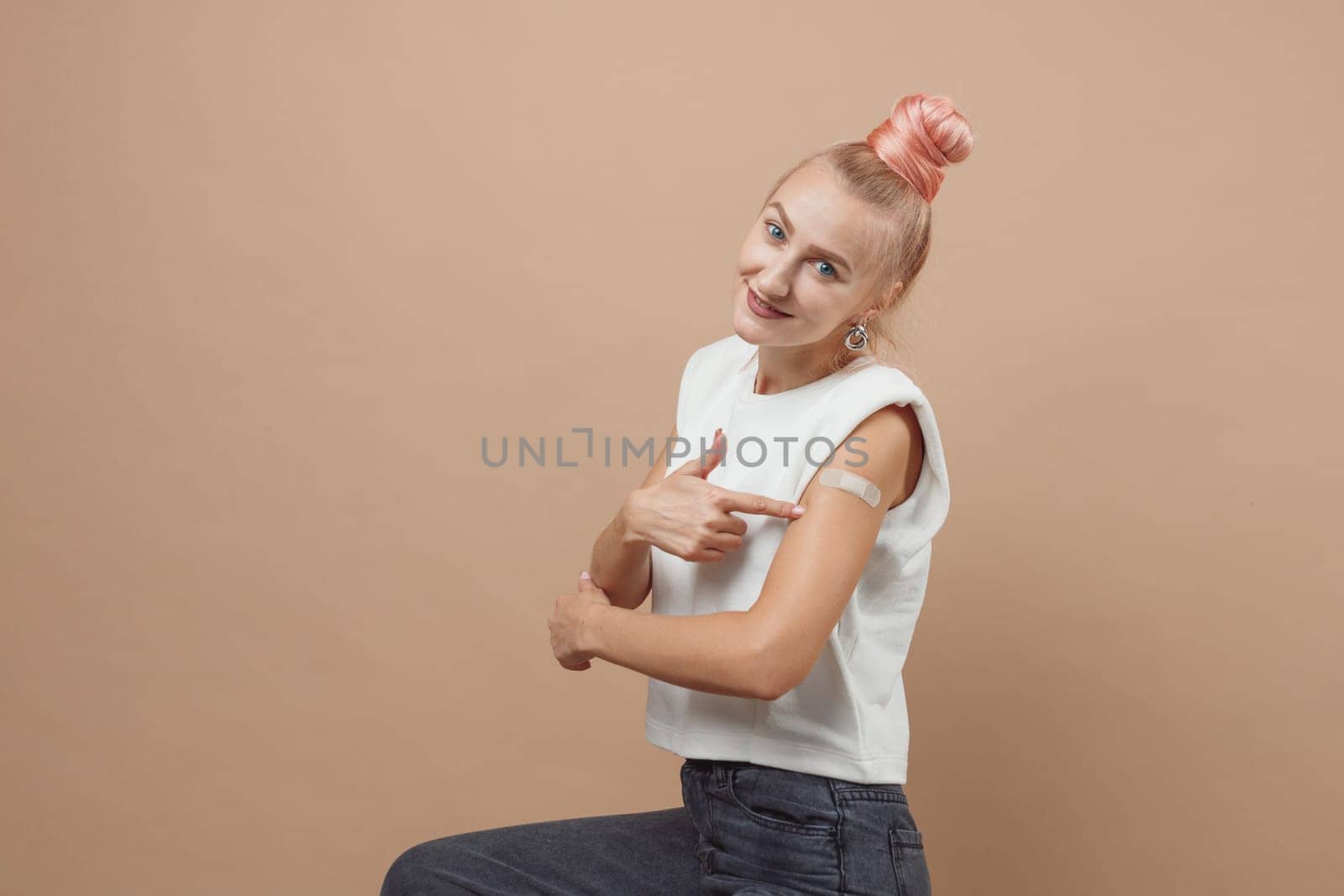 Young hipster woman with band aid after coronavirus Covid-19 vaccine injection. Covid vaccination concept, plain color background