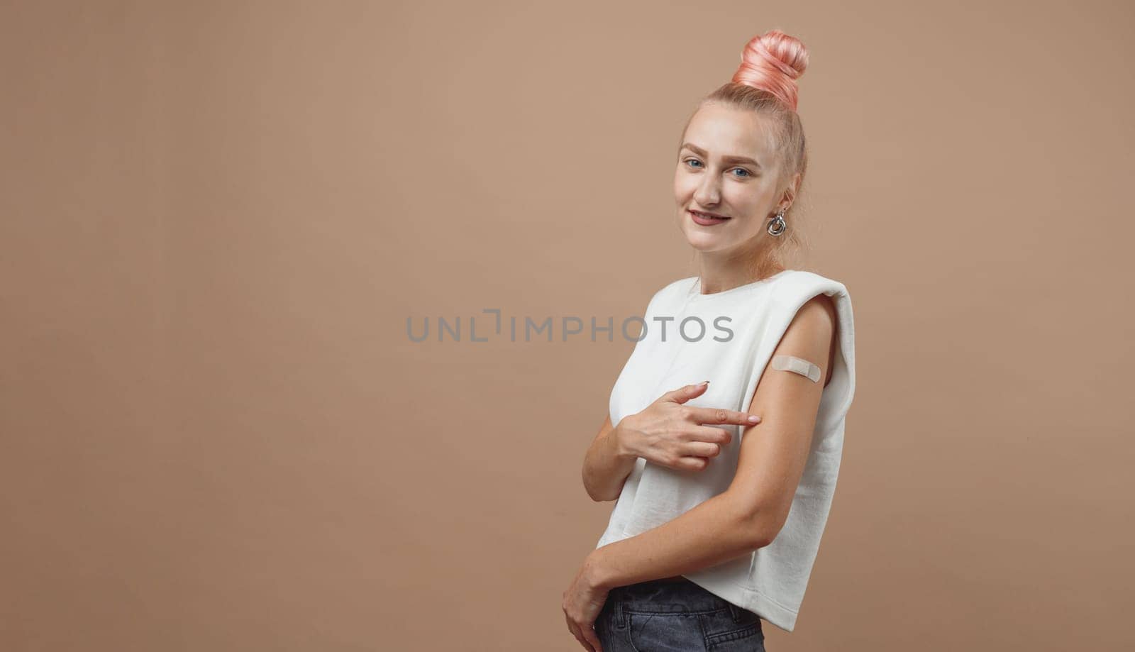 Young hipster woman with band aid after coronavirus Covid-19 vaccine injection. Covid vaccination concept, plain color background