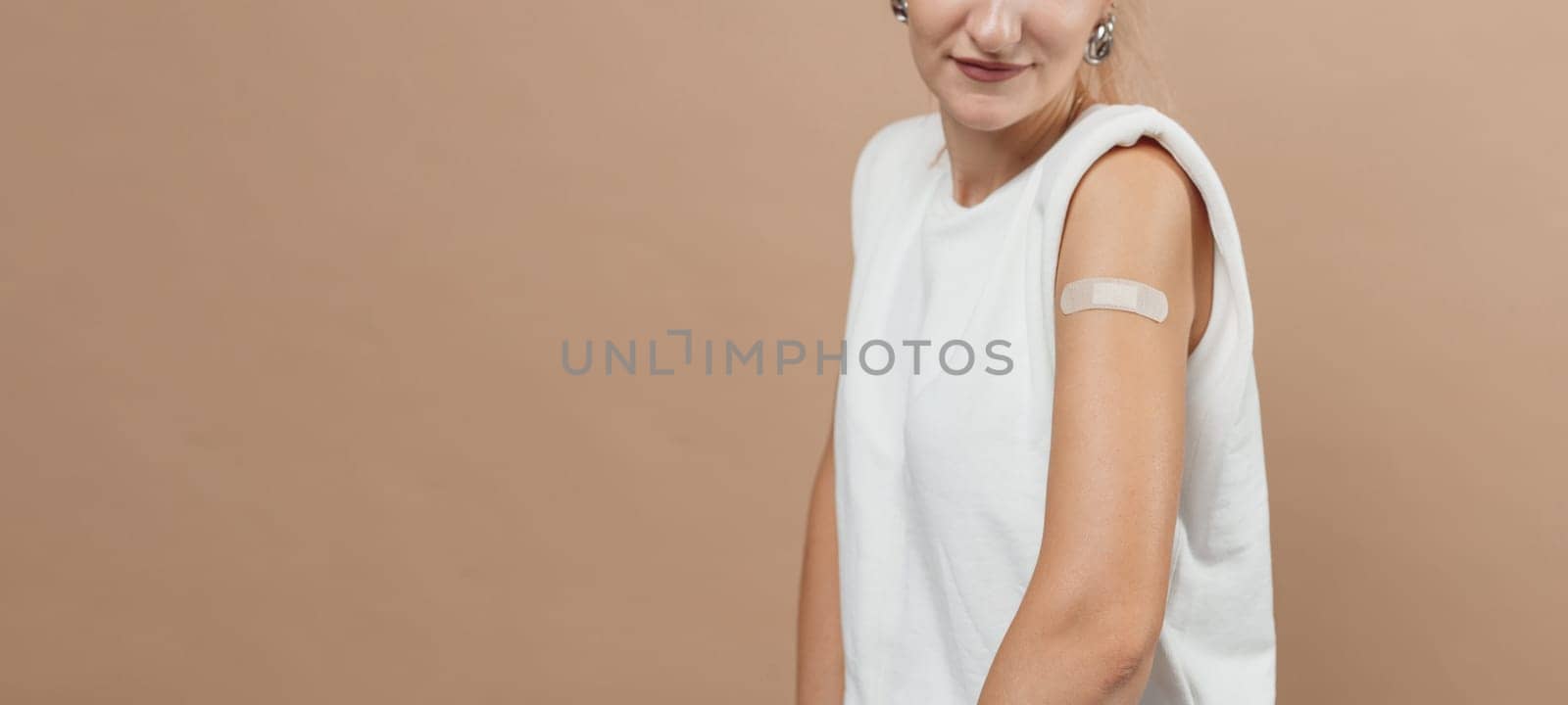 Young hipster woman with band aid after coronavirus Covid-19 vaccine injection. Covid vaccination concept, plain color background