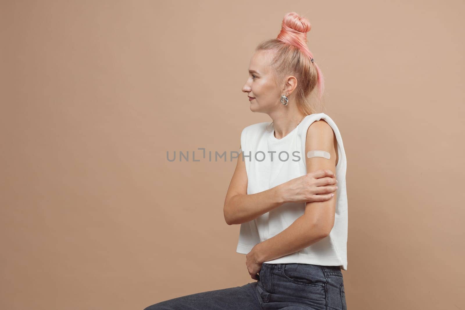 Young hipster woman with band aid after coronavirus Covid-19 vaccine injection. Covid vaccination concept, plain color background