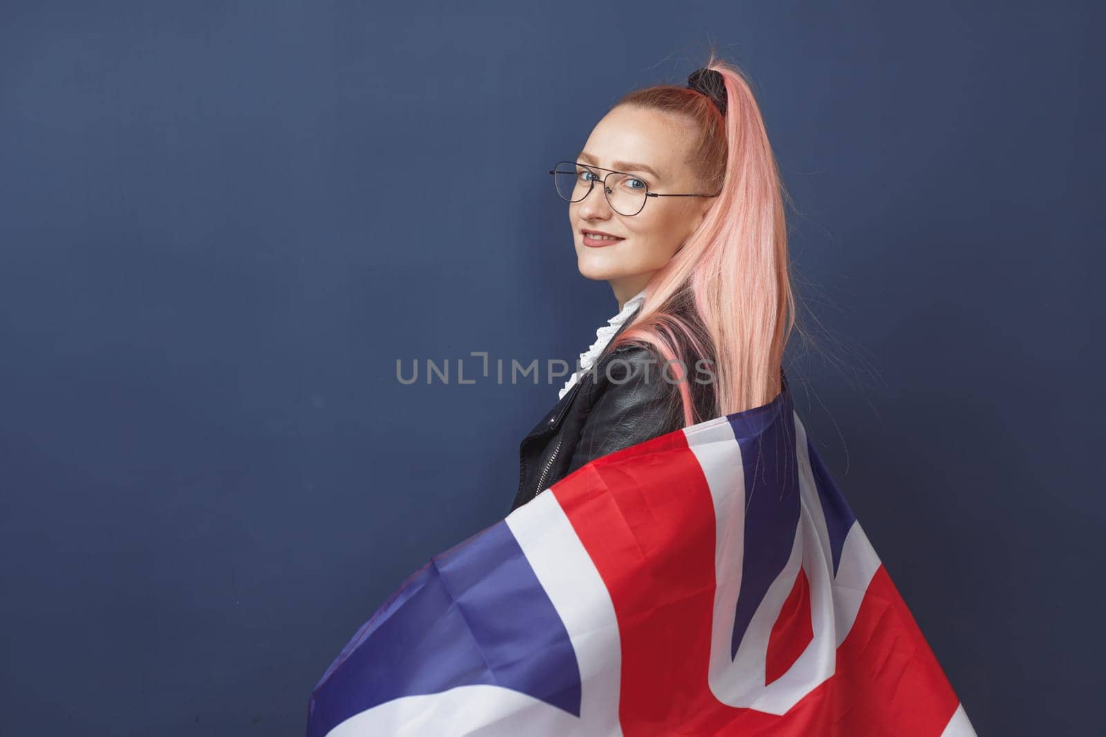 Young woman expat in eyeglasses with great britain flag. Studio shot. English language hipster teacher. Fashionly dressed woman with pink hairs in black leaher jacket and white blouse. Autumn style