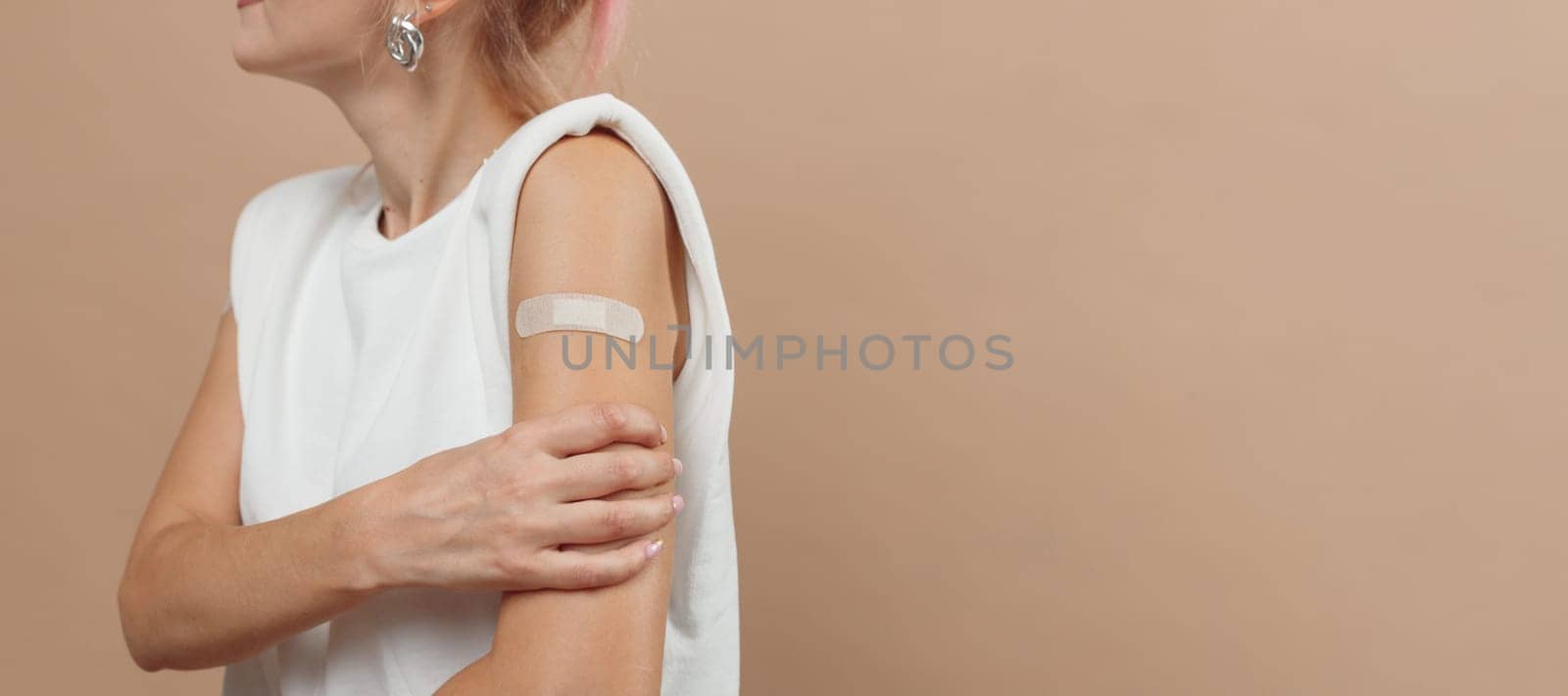 Young hipster woman with band aid after coronavirus Covid-19 vaccine injection. Covid vaccination concept, plain color background