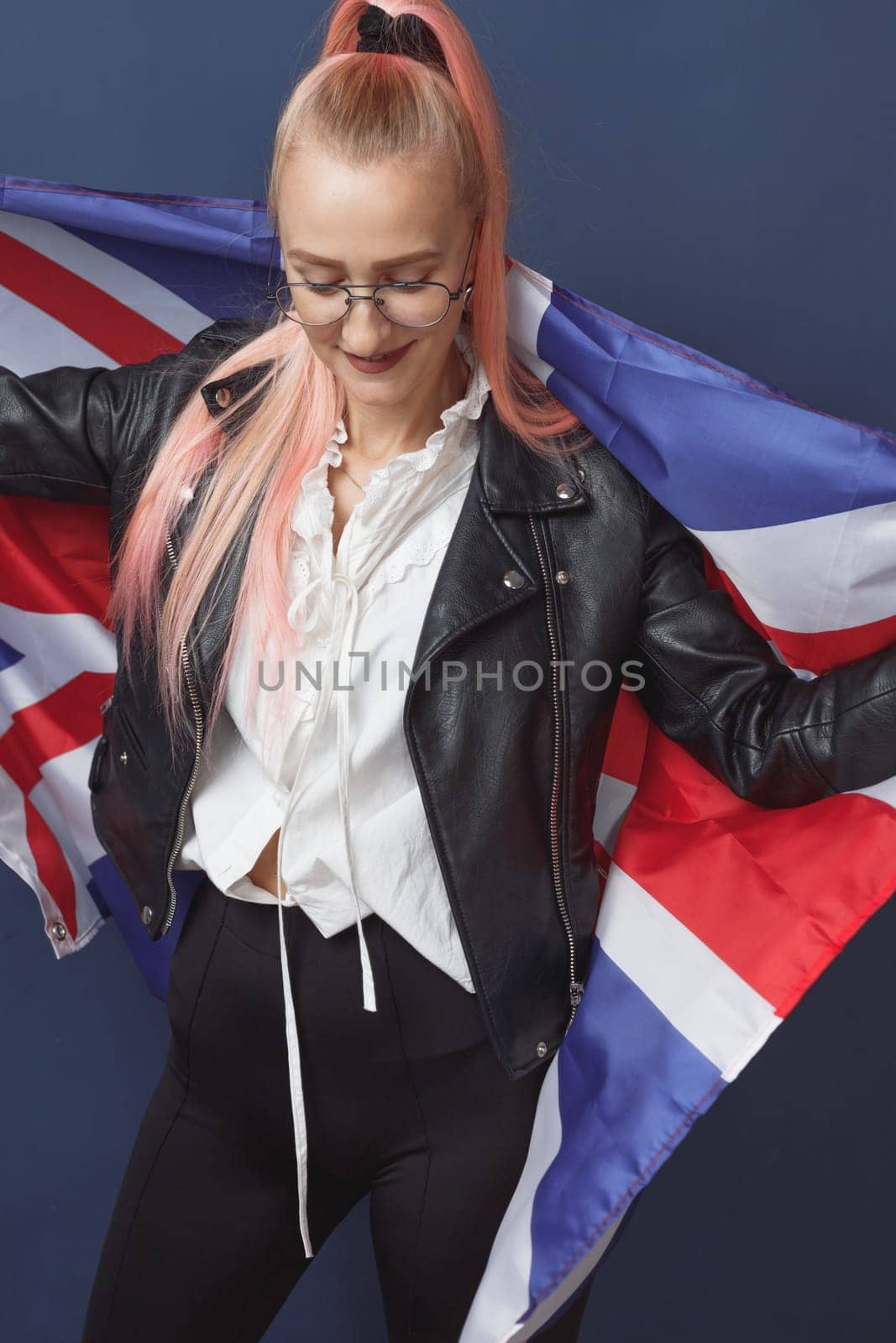 Young woman expat in eyeglasses with great britain flag. Studio shot. English language hipster teacher. Fashionly dressed woman with pink hairs in black leaher jacket and white blouse. Autumn style
