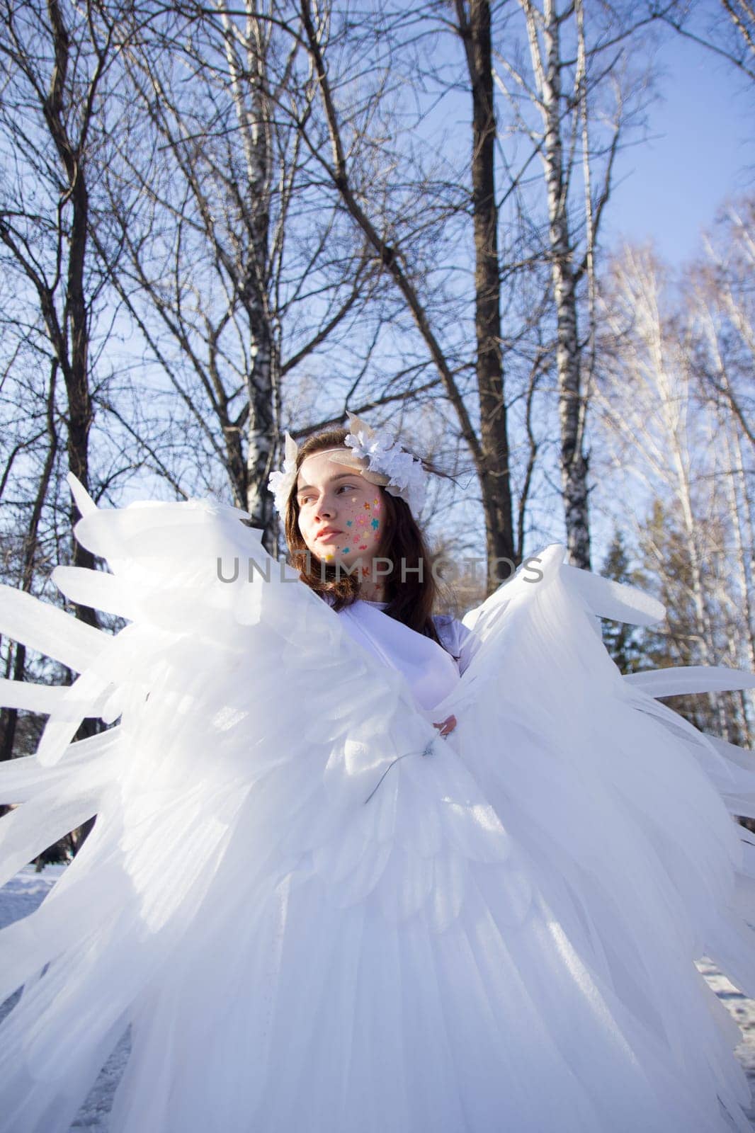 A beautiful angel by the river in winter against the blue sky.