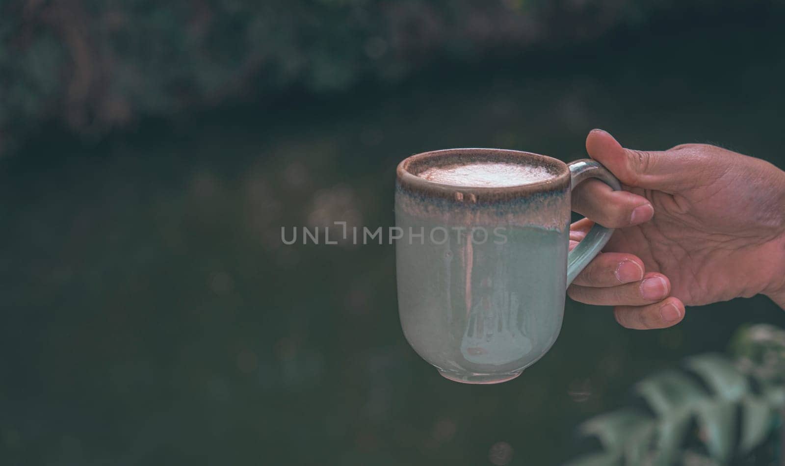 Hands of a man or barista holding cup of hot coffee latte with heart shaped foam art