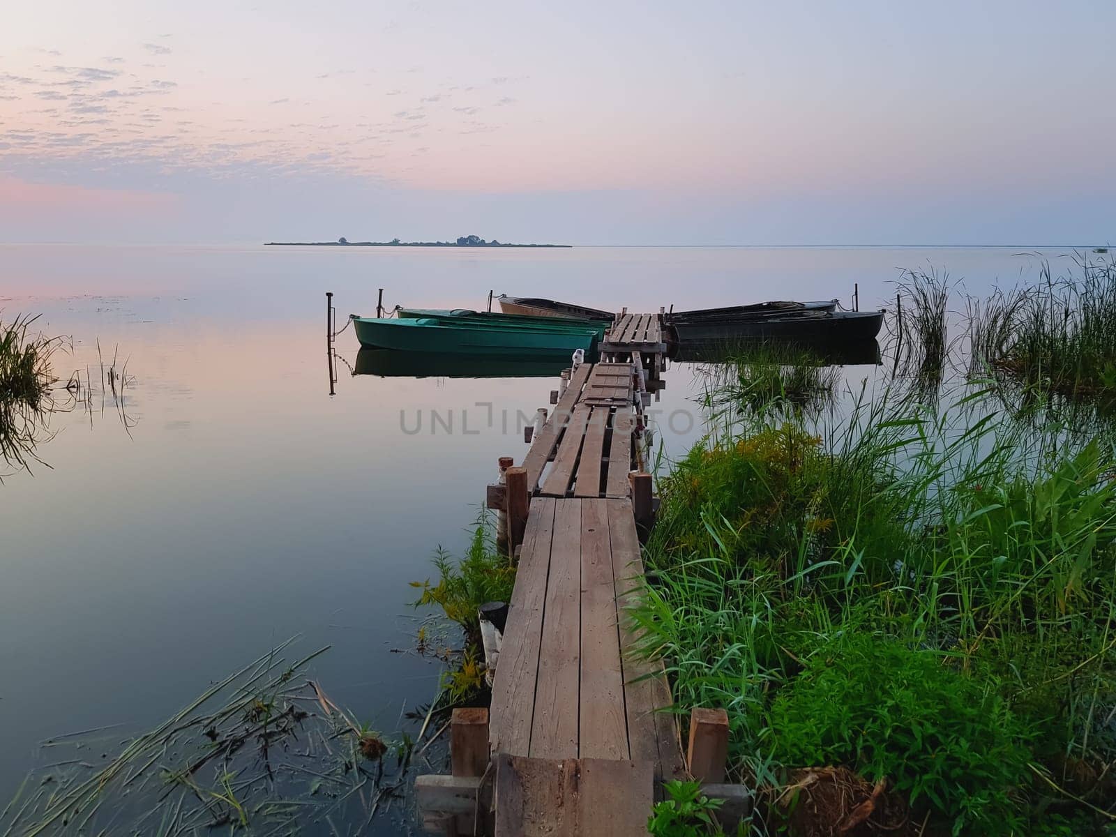 Quiet dawn in lilac and pink tones on the picturesque lake shore. Rowing boats are moored at a rural wooden pier. Russia, Rostov, Lake Nero. Space for copy.