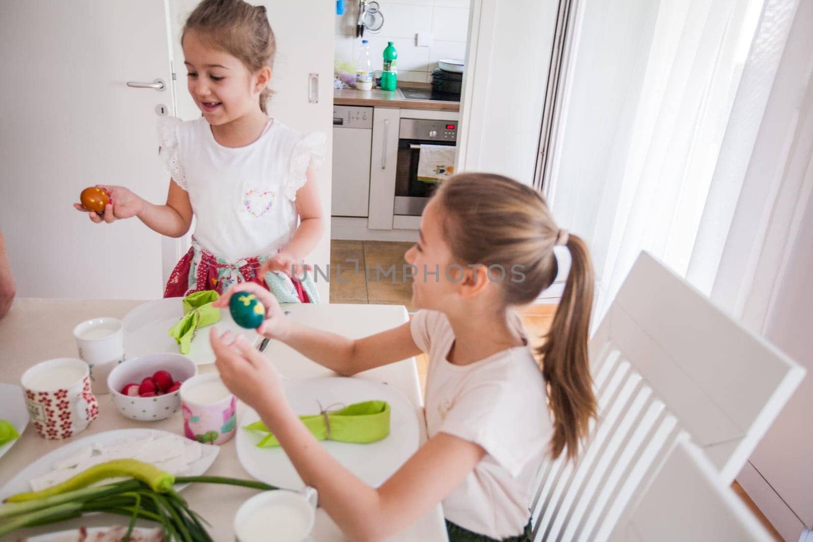 Portrait of two adorable little girls with colorful Easter eggs at home, Holiday day