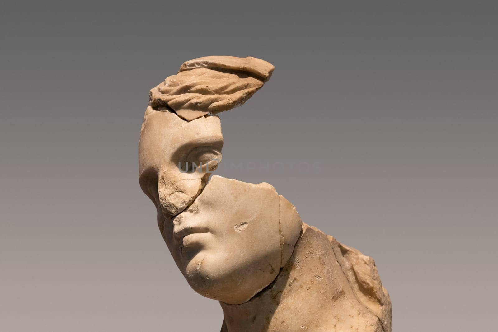 closeup portrait of antique damaged stone bust statue depicting a woman head with large pieces missing from the face area and large cracks in the marble
