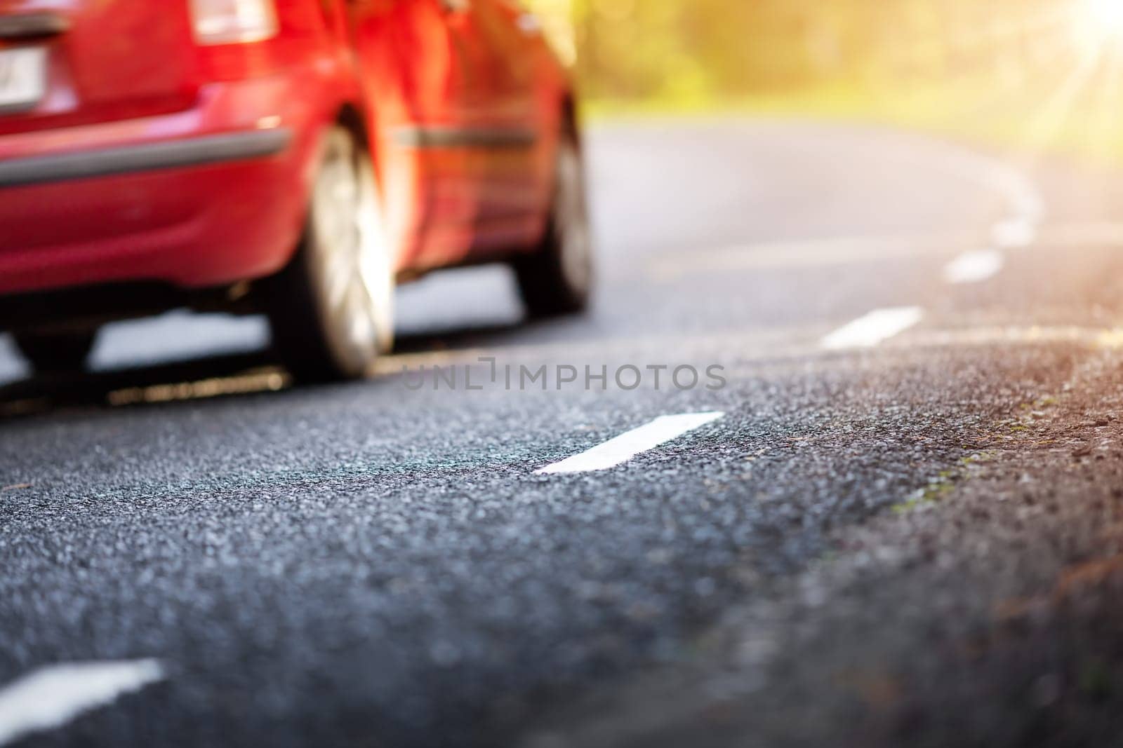 Red car on the road in the natural park. Countryside way with white dividing lines on it.