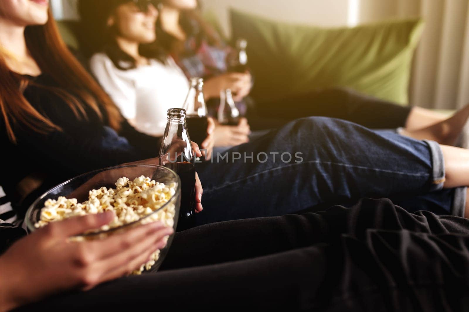 Friend group of people in 3D glasses are watching a movie, smiling, laughing. Eating and drinking while watching a movie in the cinema. Girls eat popcorn and drink soda in glass bottles. Relaxing time