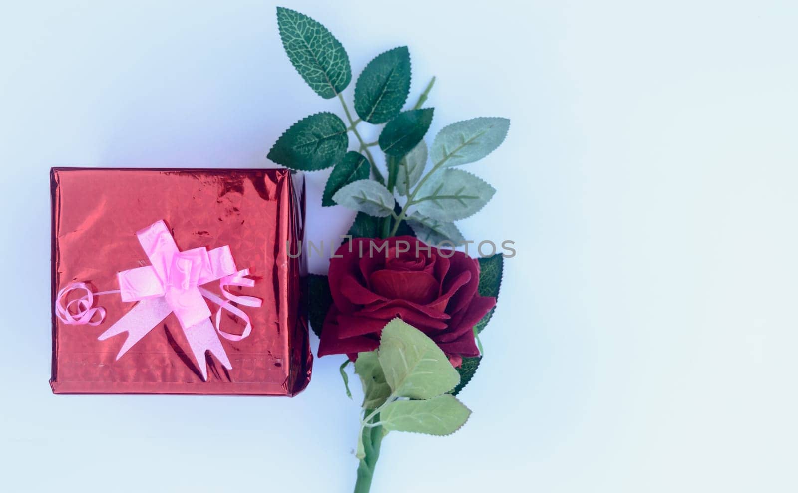 Gift box with a ribbon and a red rose in white background. Table top view. Copy Space.