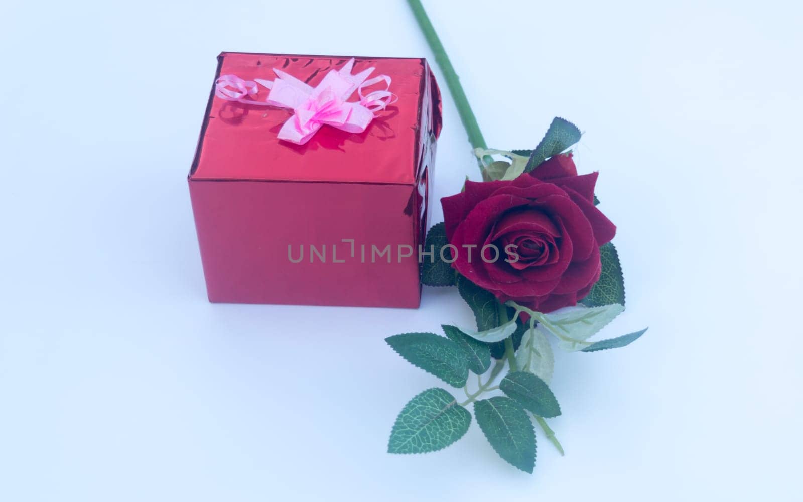 Gift box wrapped and tied with ribbon and a red rose in white background. Low angle view. Copy Space.