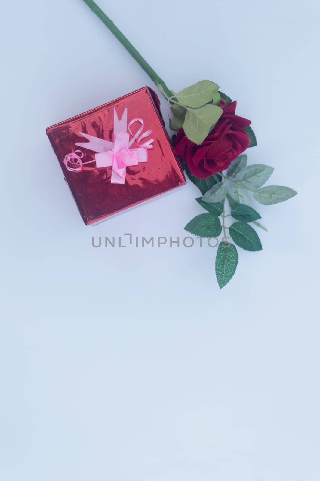 Gift box wrapped and tied with ribbon and a red rose in white background. Table top view. Vertical. Copy Space.