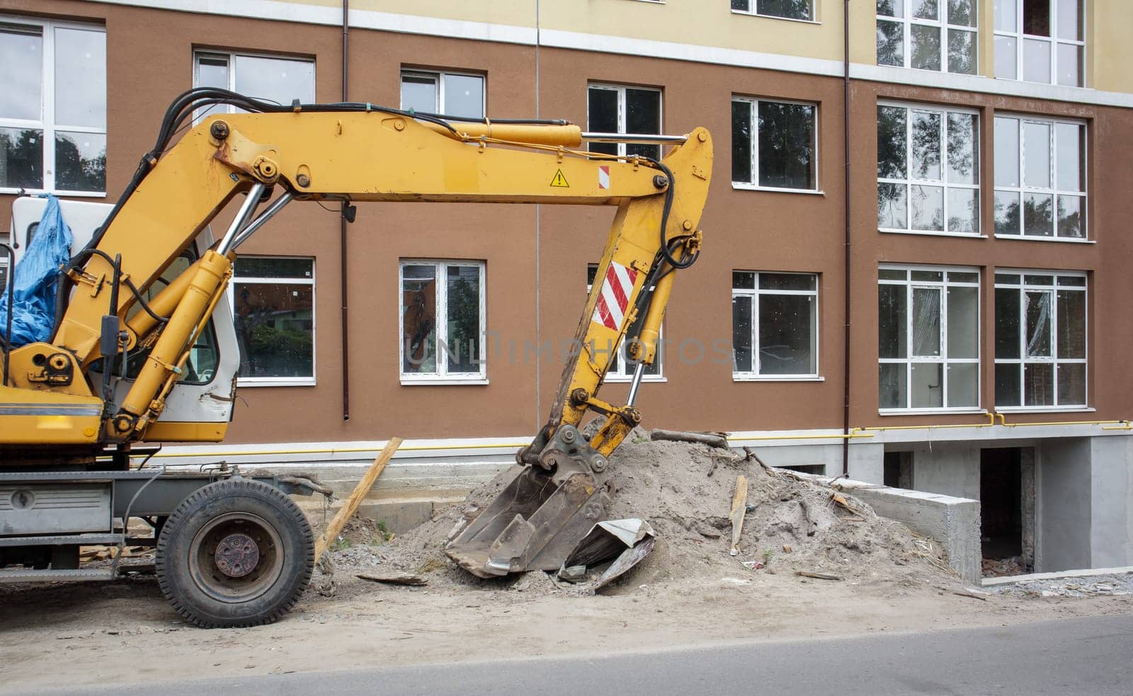 Mobile crane loader of yellow color on the background of a building under construction. German-Swiss international equipment manufacturer. The excavator is used for earthworks