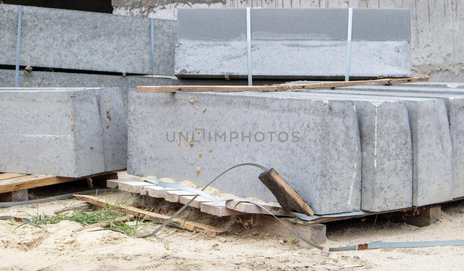 Faceted granite curbs on a pallet. Smooth porcelain stoneware products at the construction site. Curbstone, a stack of concrete curb boards prepared for installation. Road repair