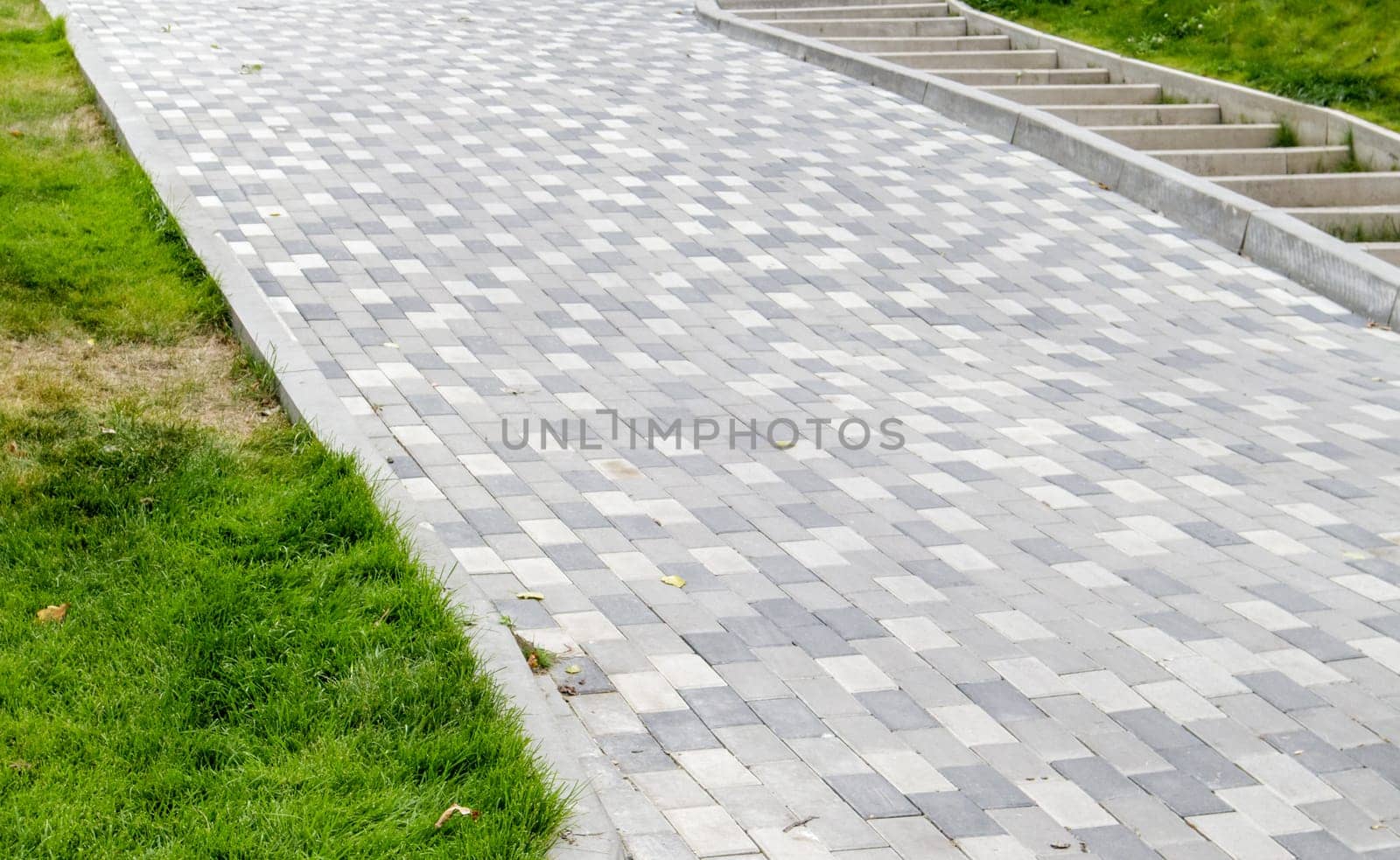 A long descent covered with gray paving slabs. The ramp is paved with concrete tiles. Wheelchair and bicycle accessibility concept