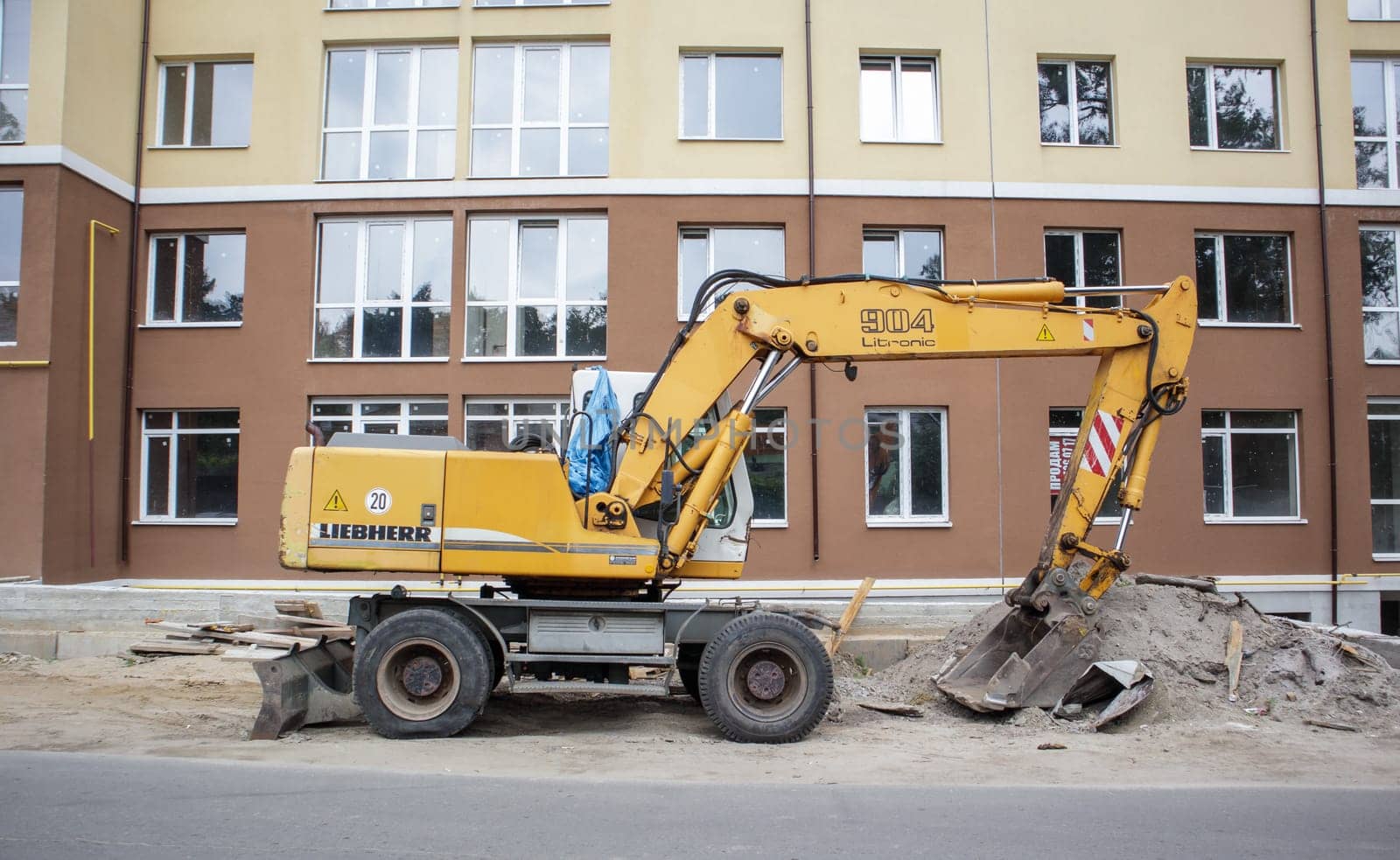 Mobile crane loader of yellow color on the background of a building under construction. International hardware manufacturer. The excavator is used for earthworks. Ukraine, Kiev - September 11, 2021