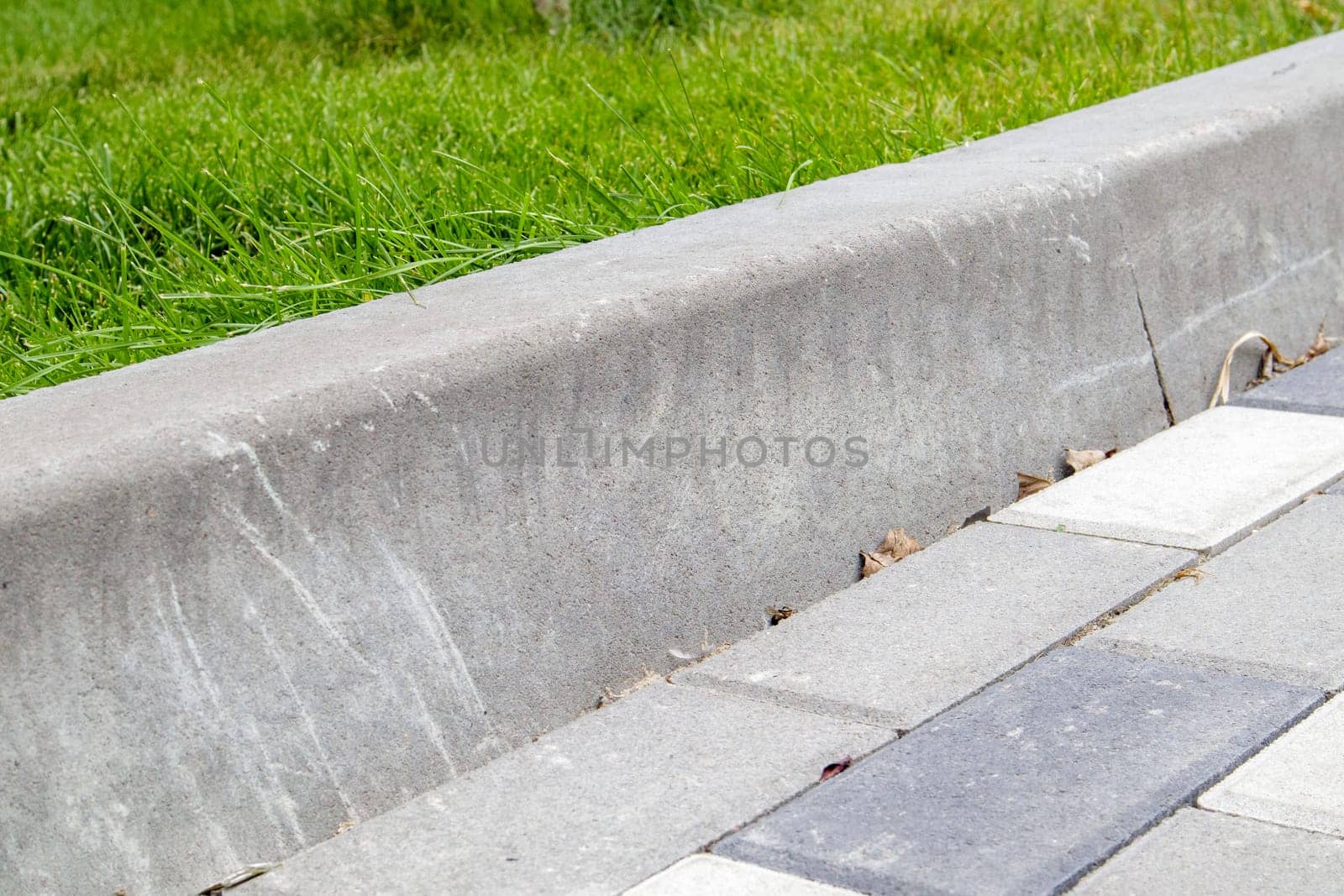 Installation of concrete curbs. Road infrastructure repair. Green grass grows near the paving slabs separated by a concrete curb. The road and the lawn are separated