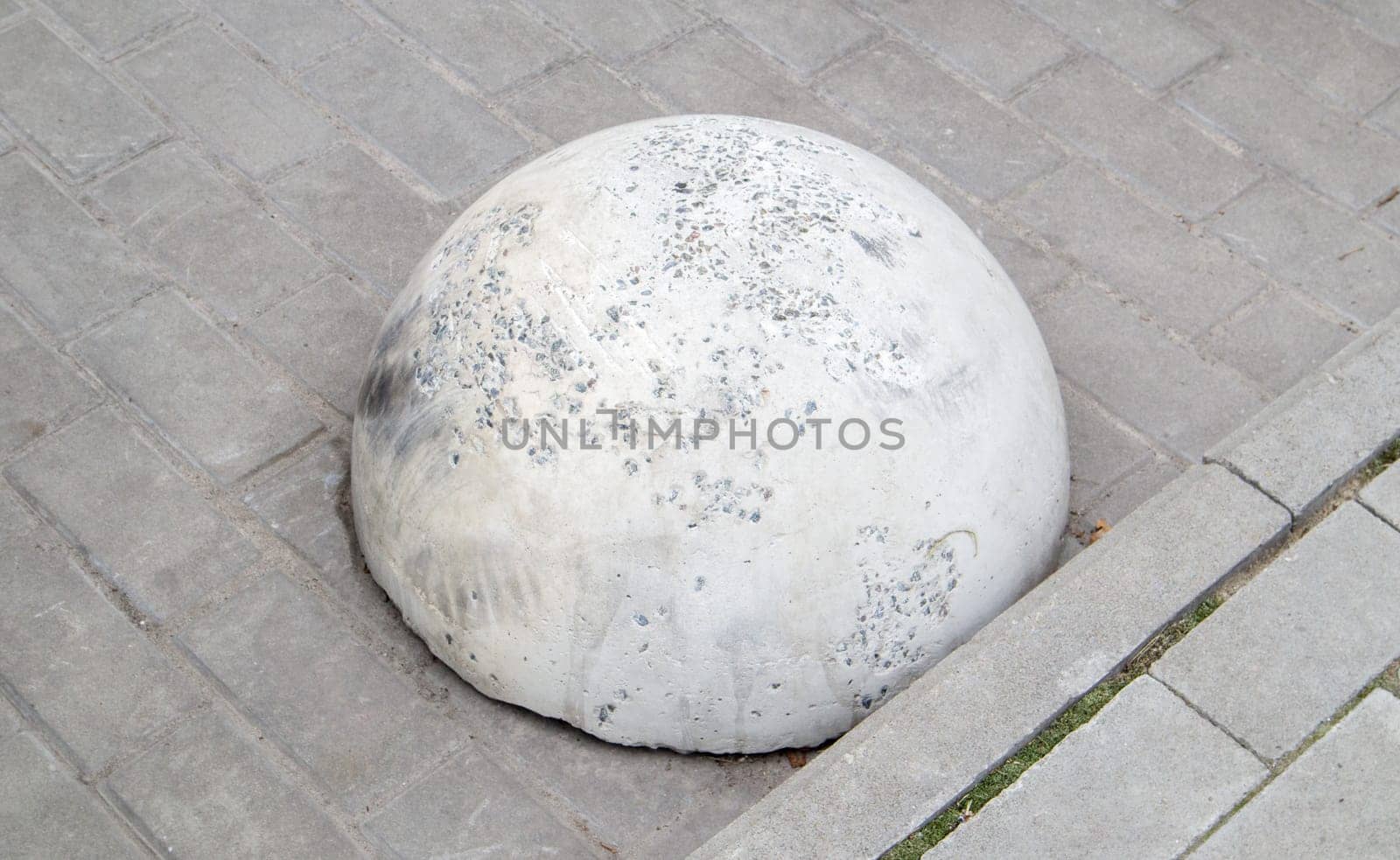 Round concrete road parking block in the shape of a hemisphere to prevent cars from parking here. Artificial obstacle for traffic and parking. Anti-parking barrier stone in the city
