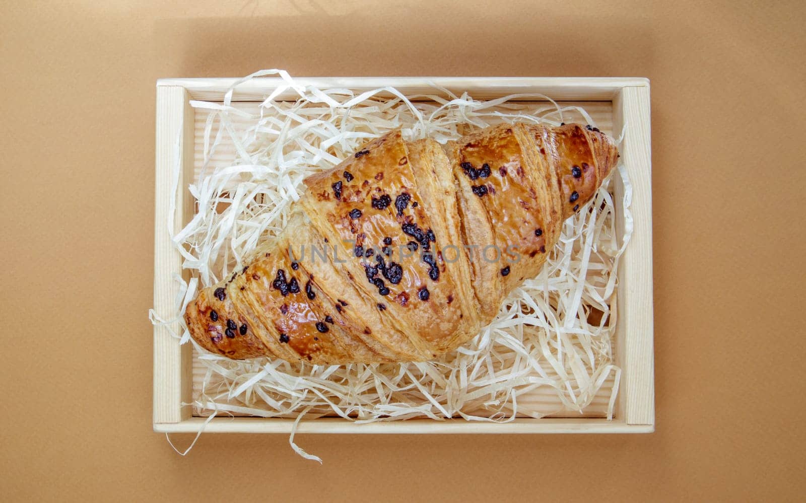One regular fresh crispy whole grain croissant with chocolate filling on a brown or coffee background with copy space. Classic traditional freshly baked French dessert, pastries. Top view, flat lay