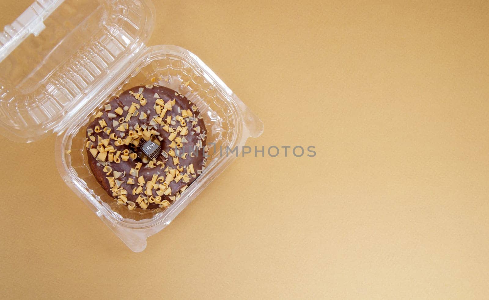Chocolate donut in a plastic container on a brown or coffee background. Takeaway breakfast concept. One donut is packed in a plastic box for delivery. Sweet pastries delivered to your home. Top view