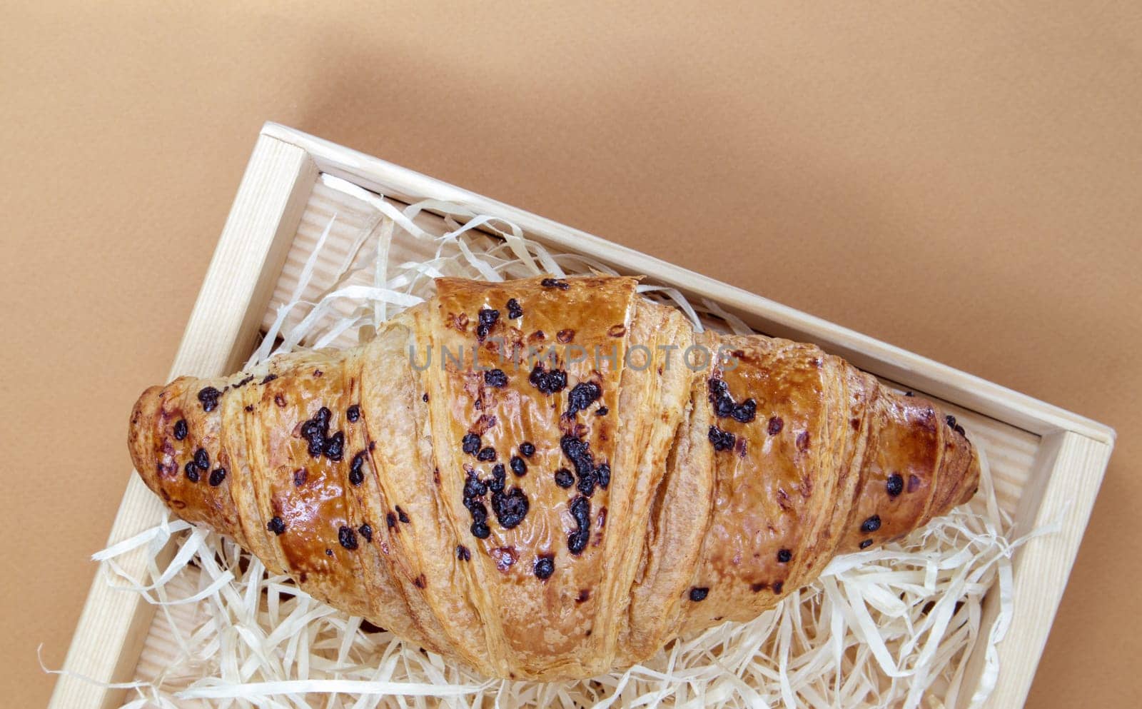 One regular fresh crispy whole grain croissant with chocolate filling on a brown or coffee background with copy space. Classic traditional freshly baked French dessert, pastries. Top view, flat lay