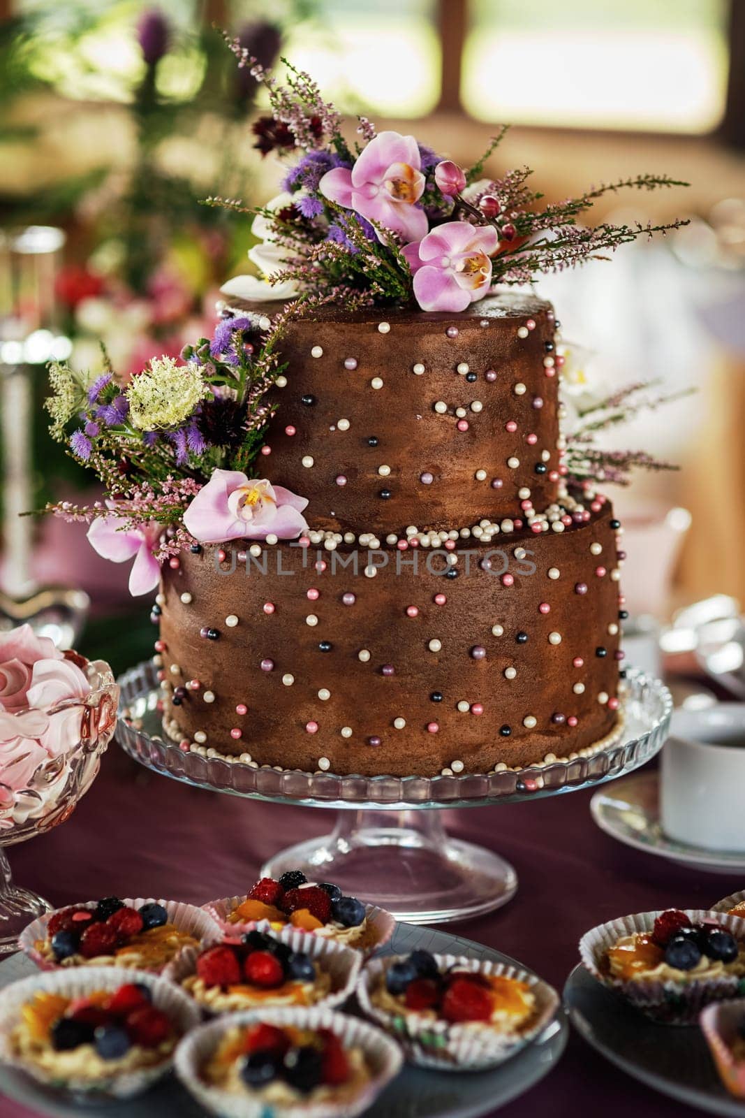 Two-tiered wedding cake beige. Decorated with handmade chocolate roses and artificial flowers. Photos in the interior. Hard light. Close-up.