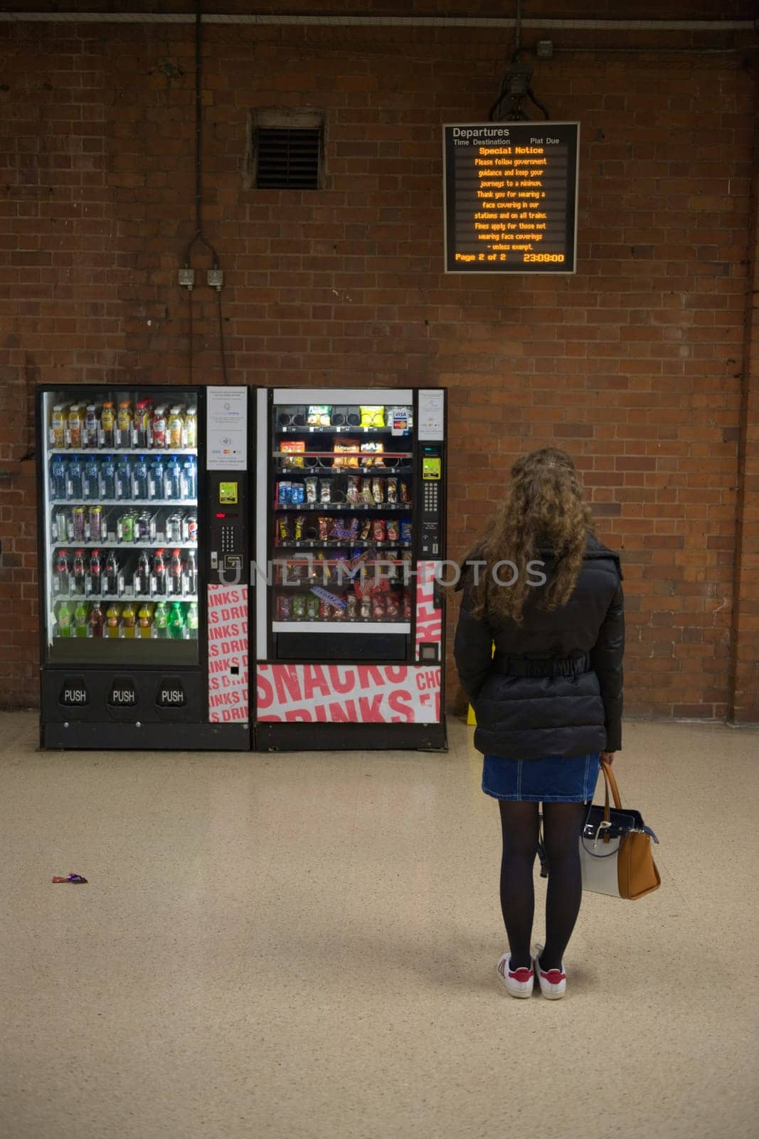 Doncaster, United Kingdom, 22nd May, 2021: Departure board displays COVID information for rail travel, read by a young woman stood by vending machines