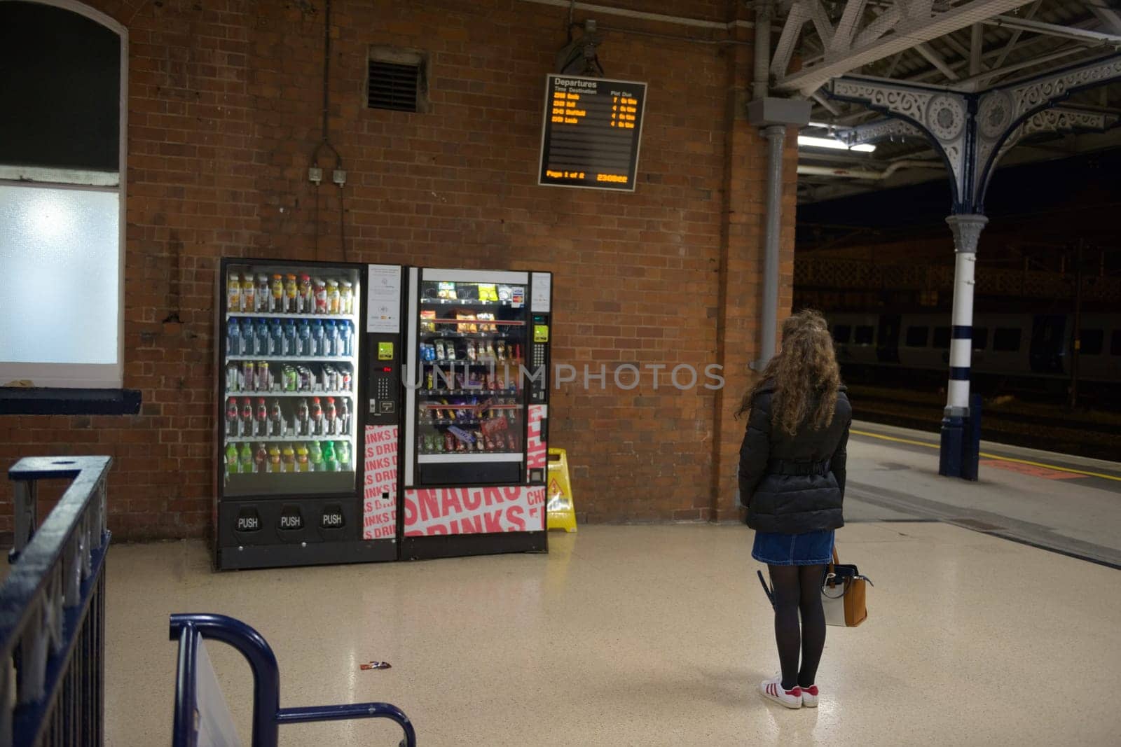 Doncaster, United Kingdom, 22nd May, 2021: Lone young woman studies doncaster train station departure board at night time following a cancellation