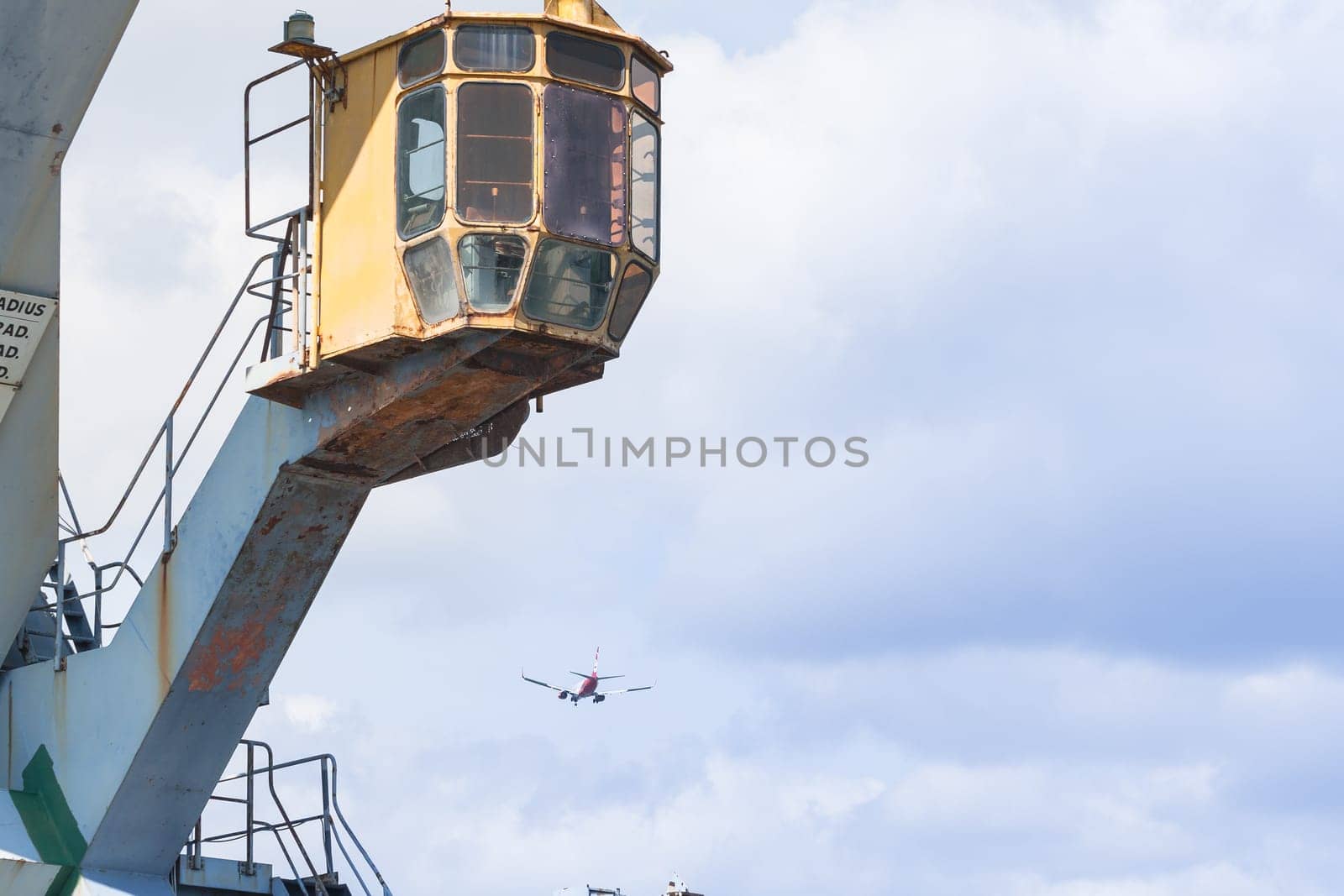 Particular of a Old crane at the dock of the port with airplane in background