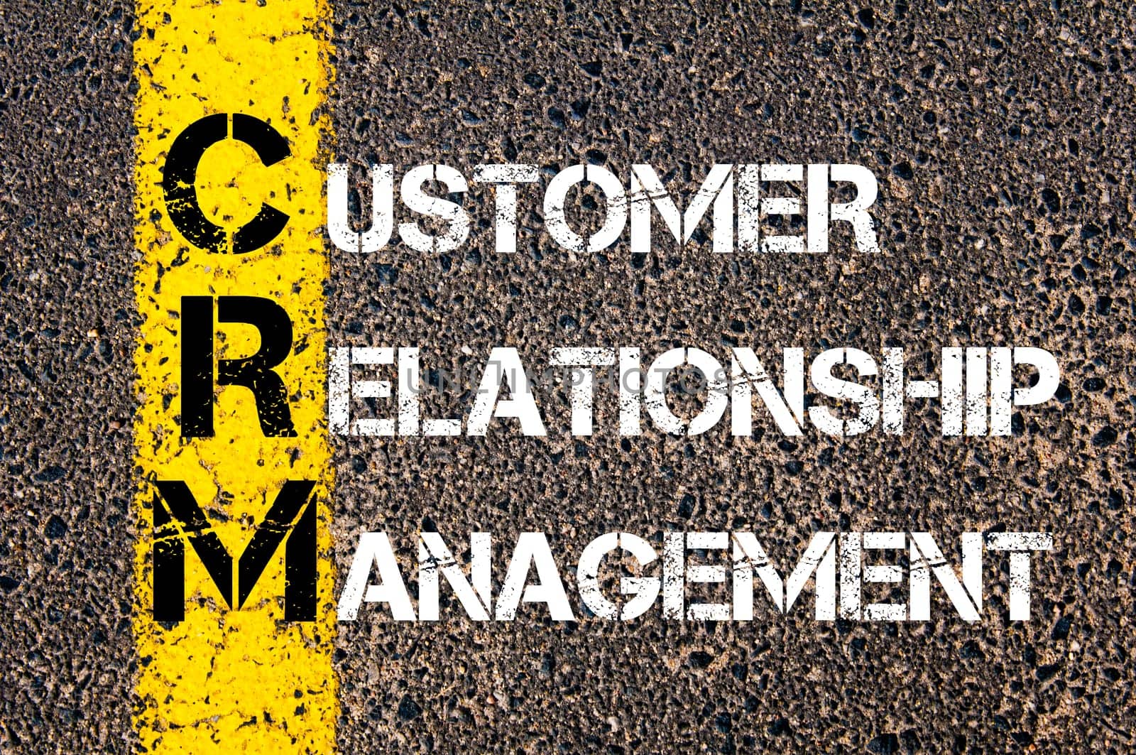 Acronym CRM - Customer Relationship Management. Business Conceptual image with yellow paint line on the road over asphalt stone background.