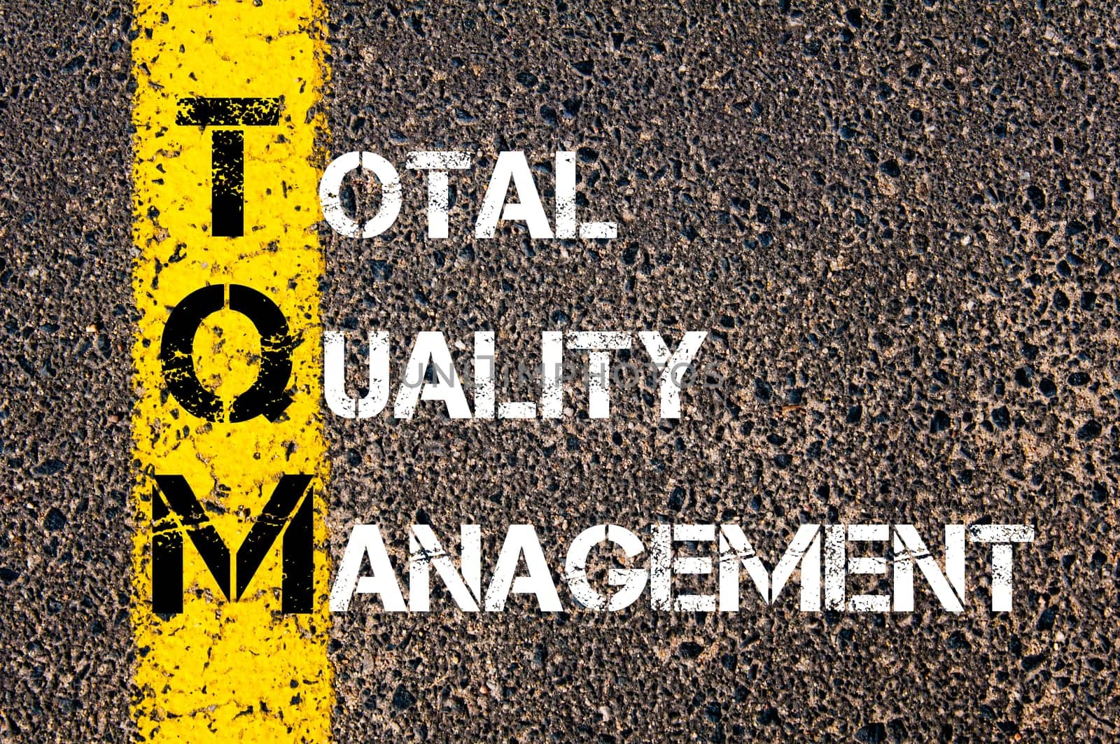 Acronym TQM - Total Quality Management. Business Conceptual image with yellow paint line on the road over asphalt stone background.