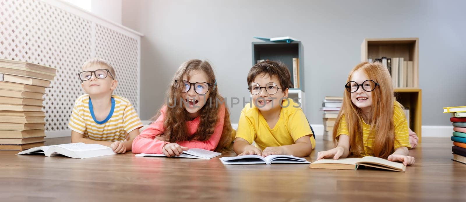 Four cute children in glasses lying on the floor indoors with books. Concept of hobby and education.