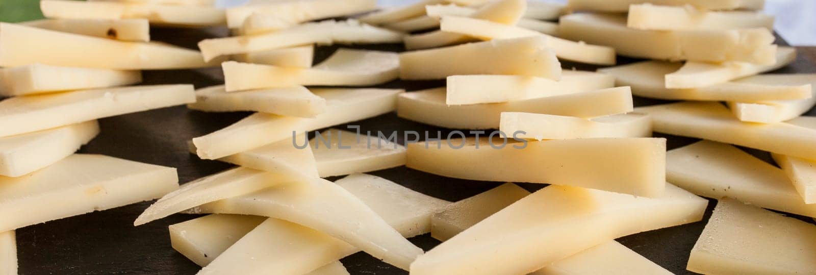 Cured slices of manchego cheese over black slate tray. Closeup